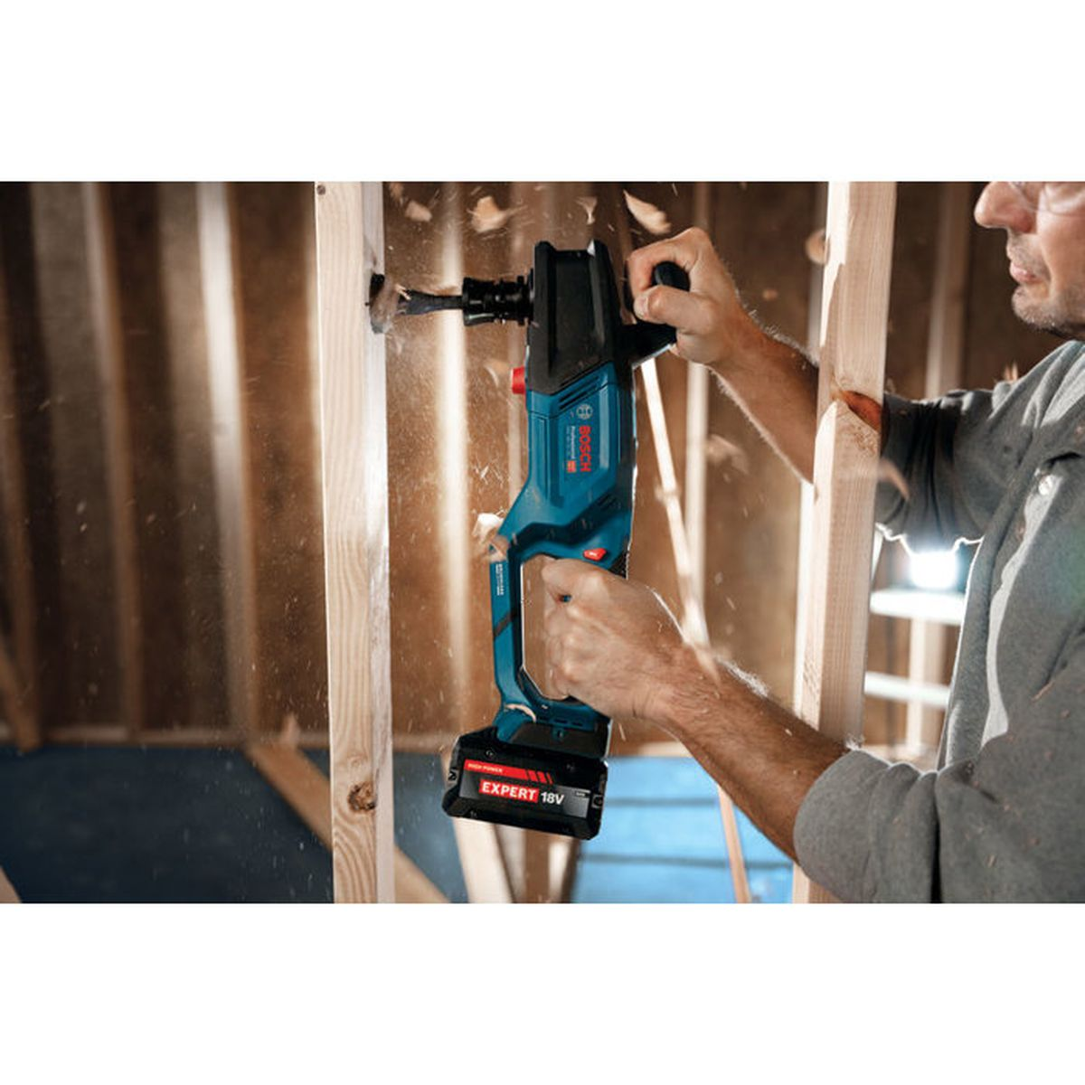 Un hombre taladra un marco de madera con un taladro inalámbrico Bosch azul.