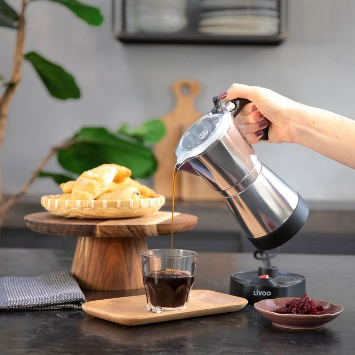 Caffè versato dalla moka in un bicchiere, con croissant e bacche secche.