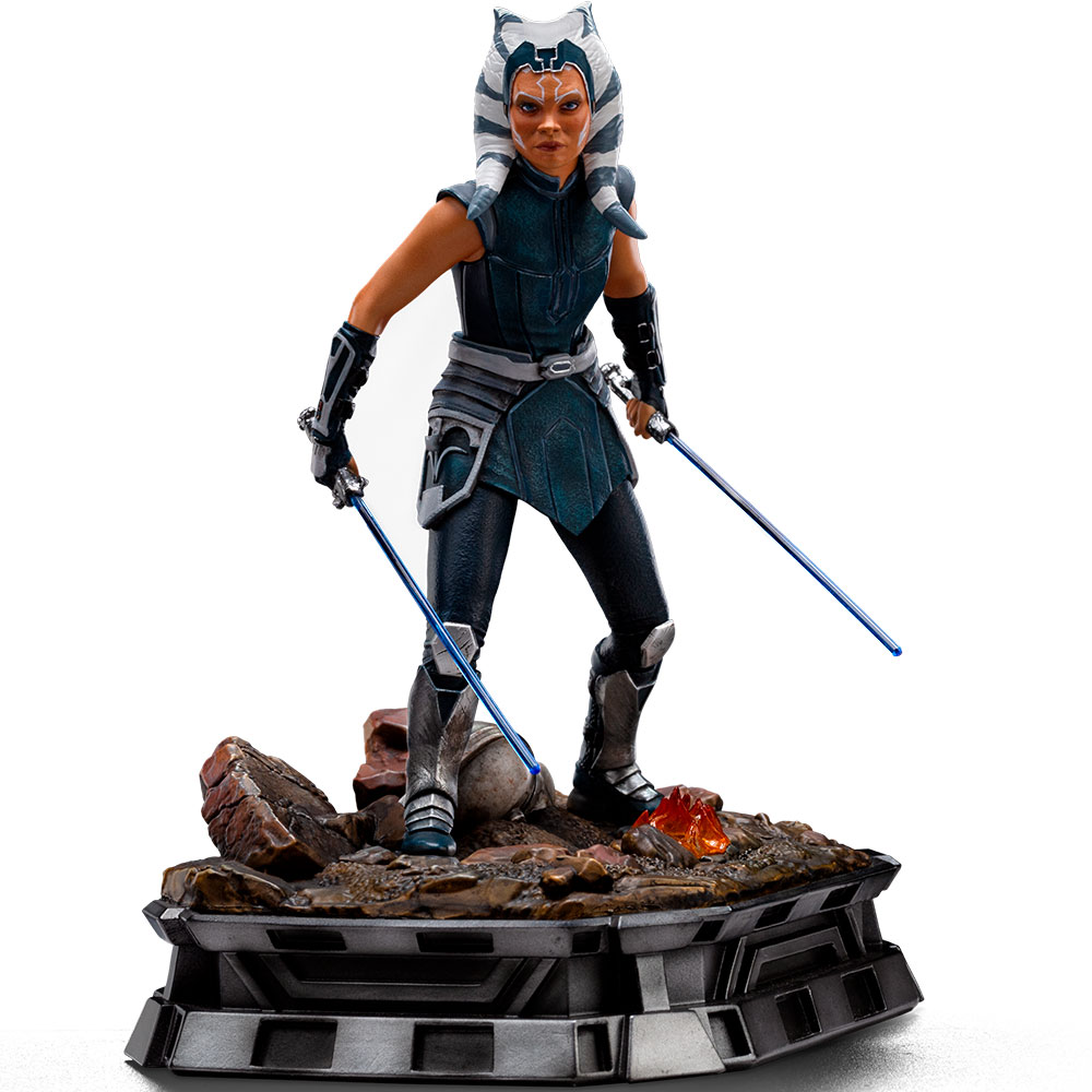 Figur einer Frau mit blauen Lichtschwertern auf felsigem Sockel.