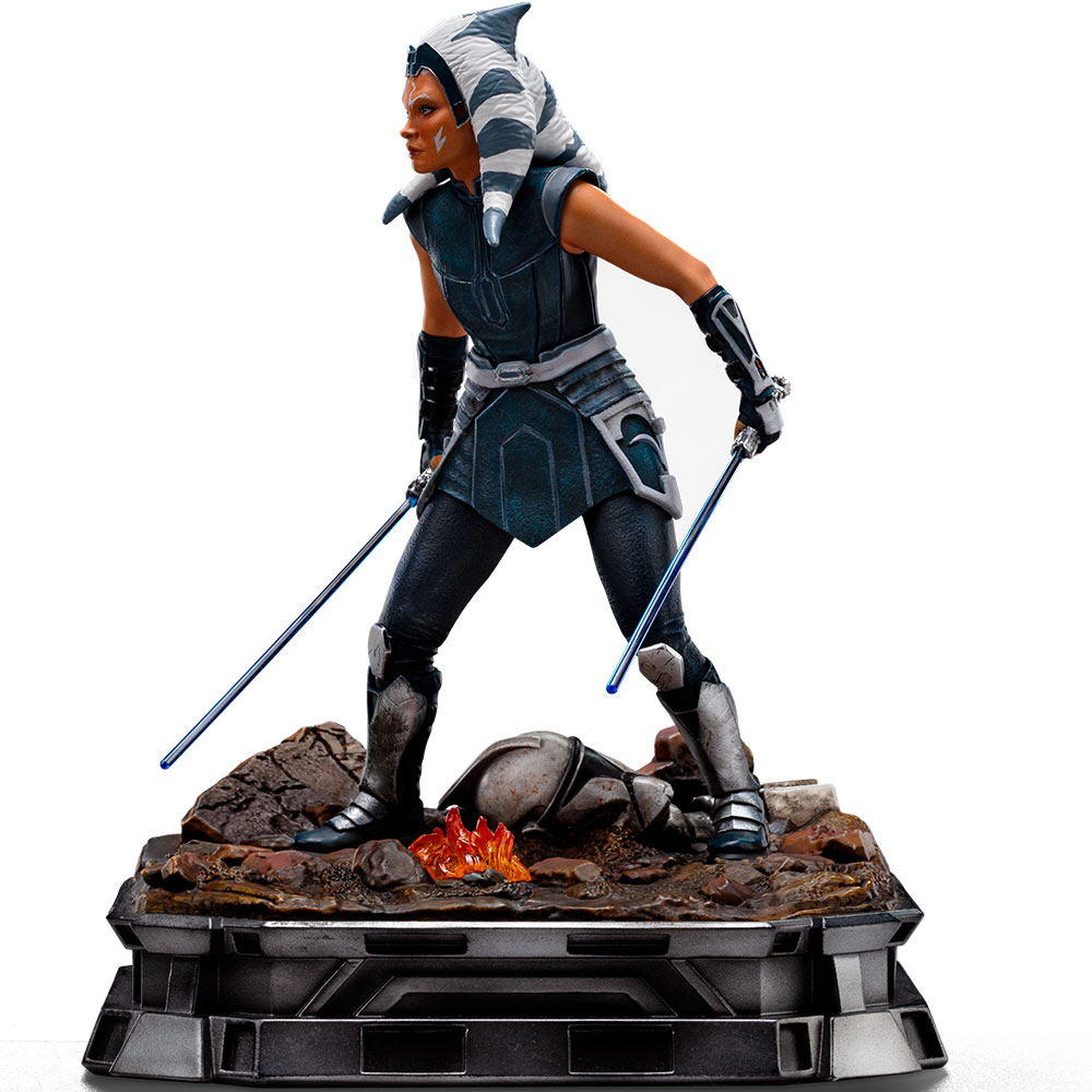 Eine Statue von Ahsoka Tano hält zwei blaue Lichtschwerter und steht auf einem felsigen Sockel.