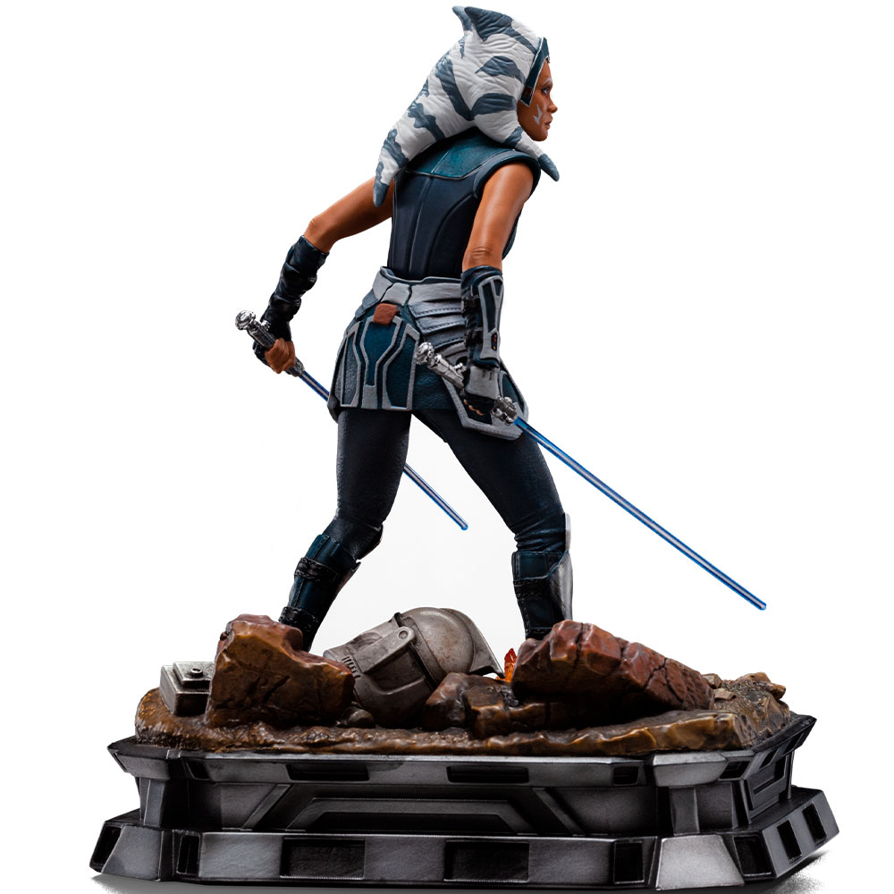 Eine Figur von Ahsoka Tano mit zwei blauen Lichtschwertern auf einem felsigen Sockel mit einem Helm.