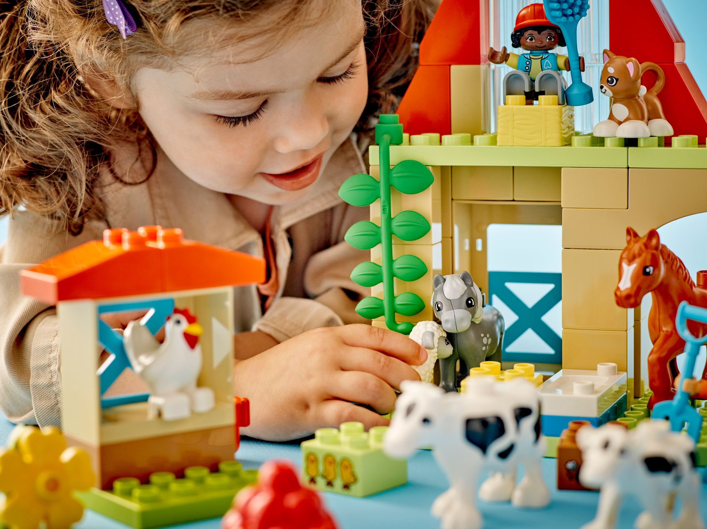Ein Mädchen spielt mit Lego-Bauernhoftieren: Hühner, Kühe, Pferd, Schaf, Hund.
