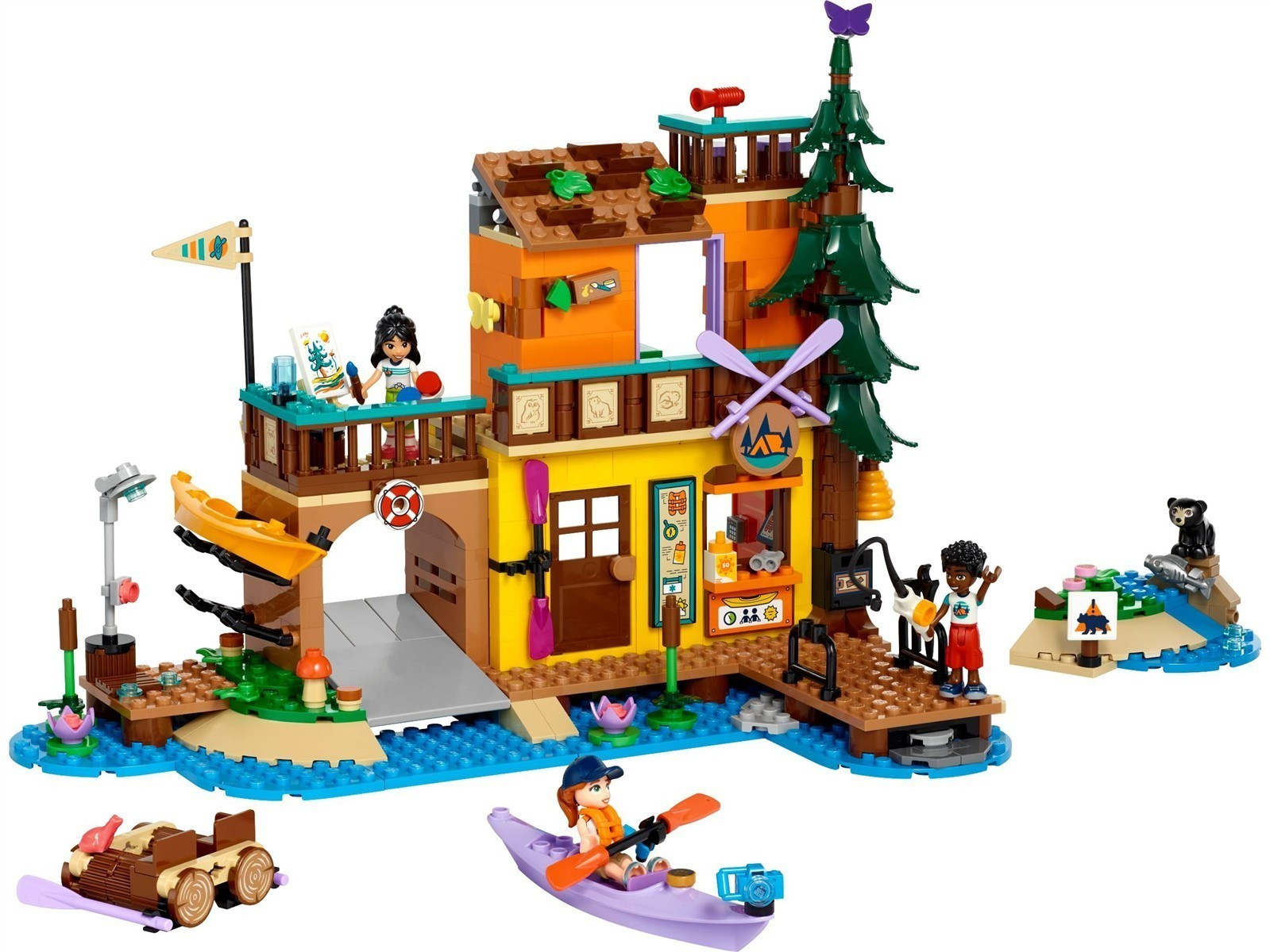 Ein Lego-Ferienhaus mit Figuren, Kajaks, einem Baum und einem Bären am Wasser.