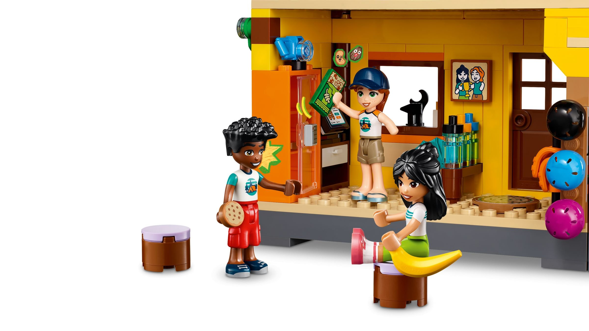 Drei LEGO Friends spielen in einem gelben Gebäude. Einer hält einen Keks, ein anderer einen Snack.