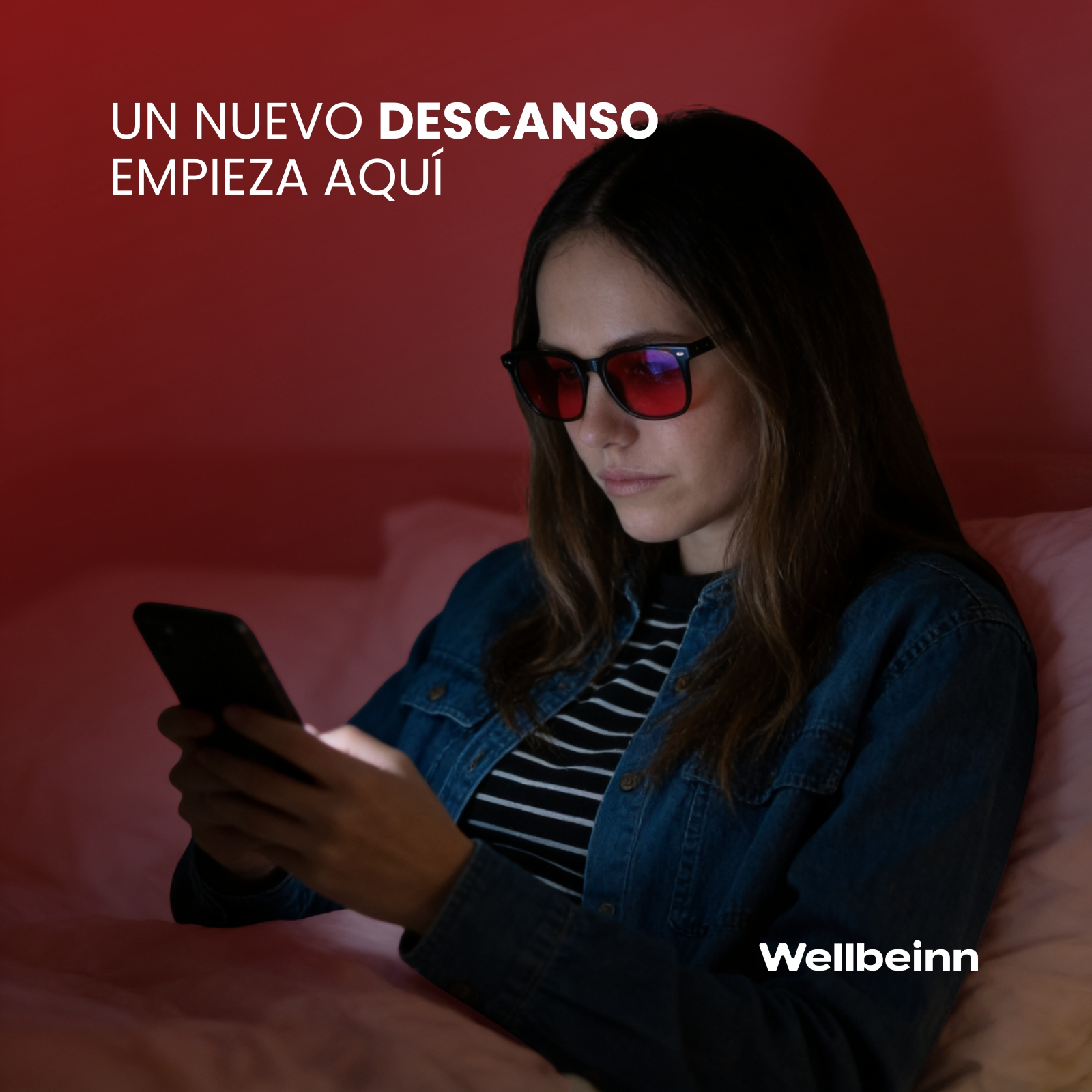 Una mujer con gafas rojas mira su teléfono. Lleva una chaqueta vaquera.