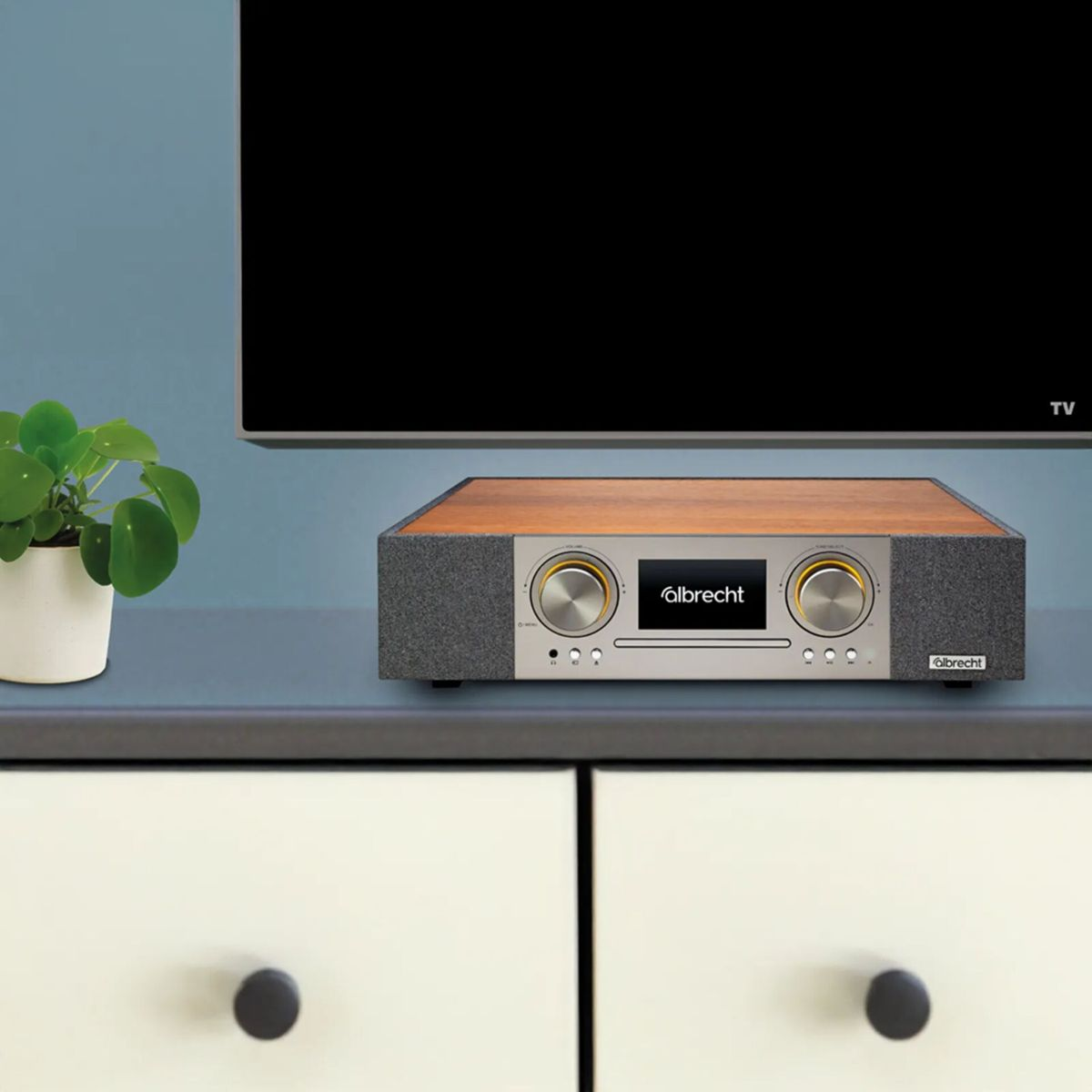 Ein Albrecht Radio mit Holzoberseite auf einem weißen Schrank unter einem schwarzen Fernsehbildschirm.