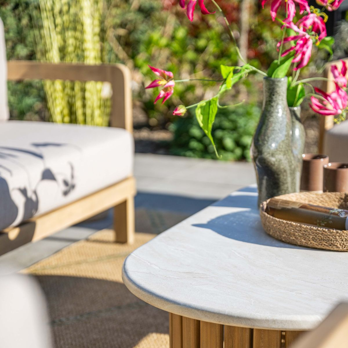 Outdoor seating area with white cushions, a table with pink flowers in a vase and a woven basket.