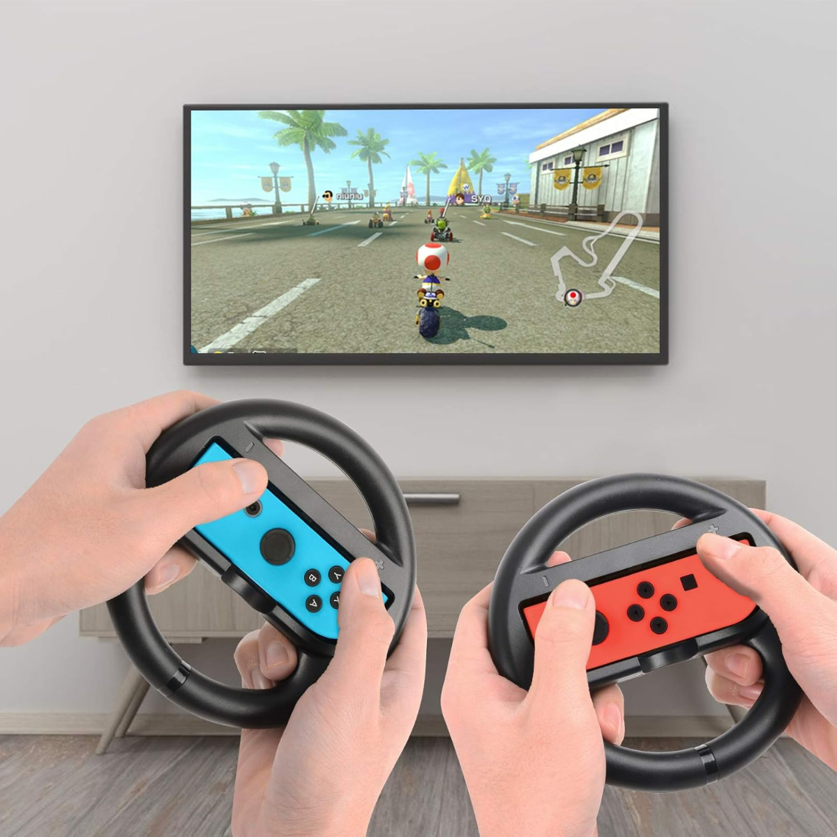 Mani tengono volanti di gioco, giocano a un gioco di corse in TV con palme.