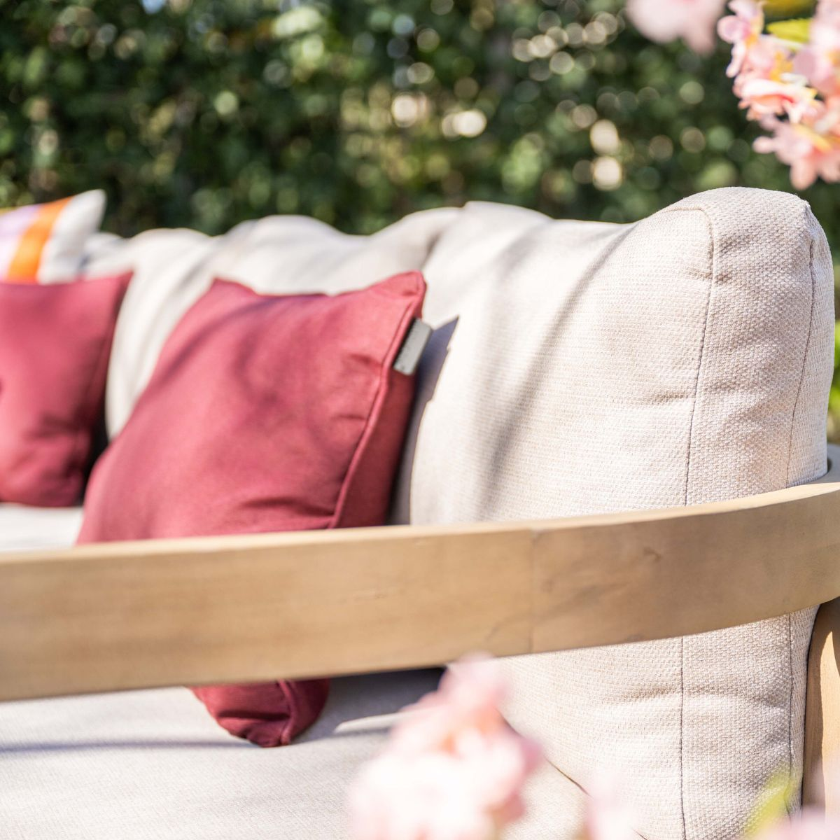 Een beige buitensofa met rode kussens en houten accenten.