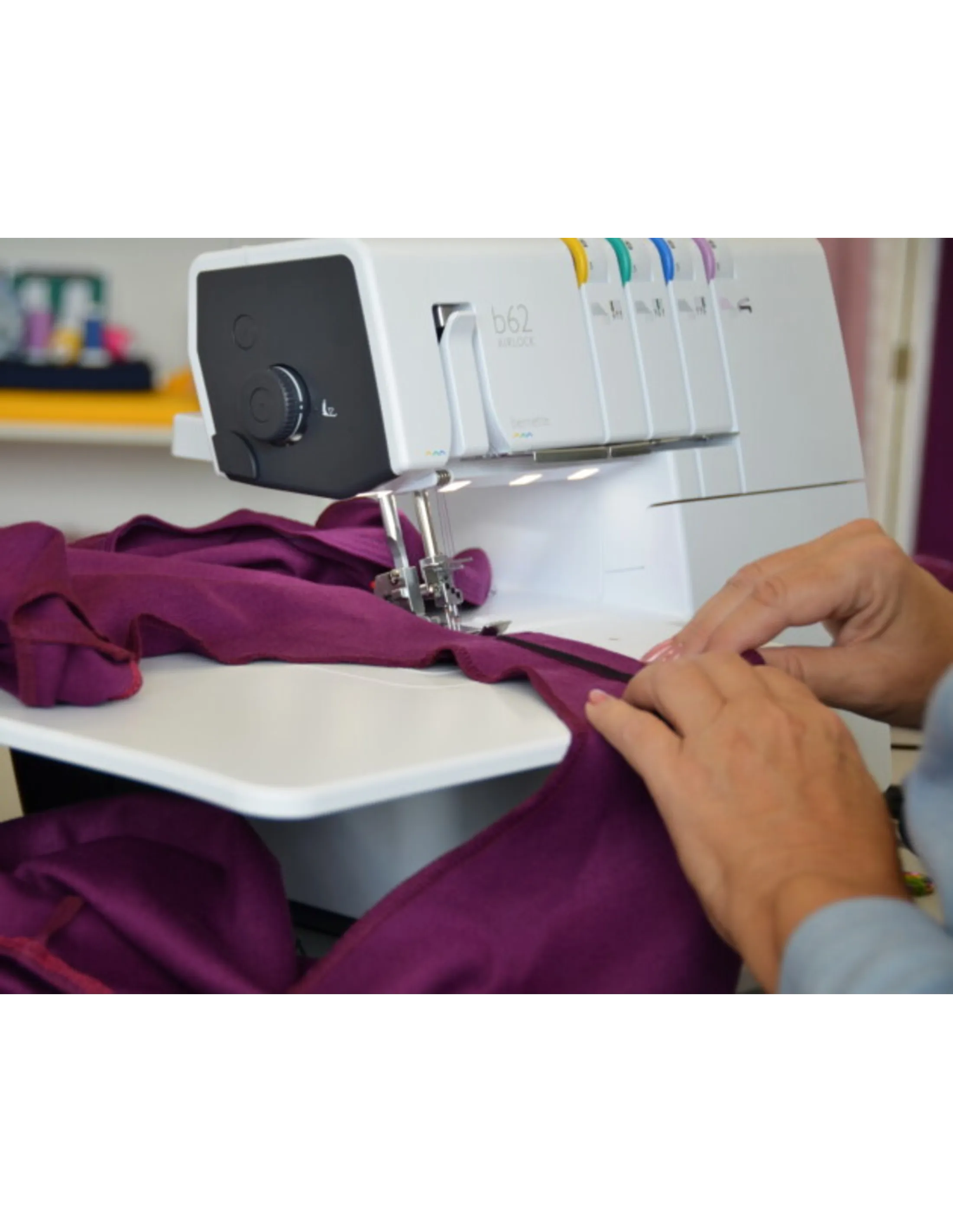 Hands sewing purple fabric with a serger sewing machine with colored threads.