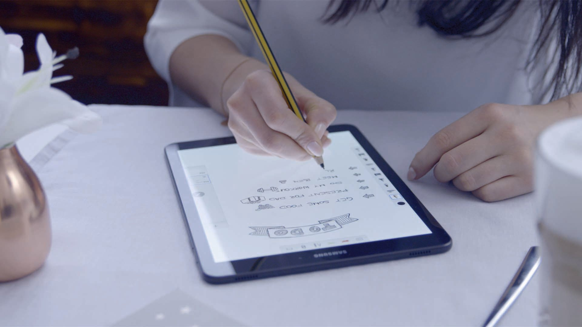 Eine Person schreibt eine To-Do-Liste auf ein Tablet mit einem Bleistift. Eine weiße Lilie ist in der Nähe.