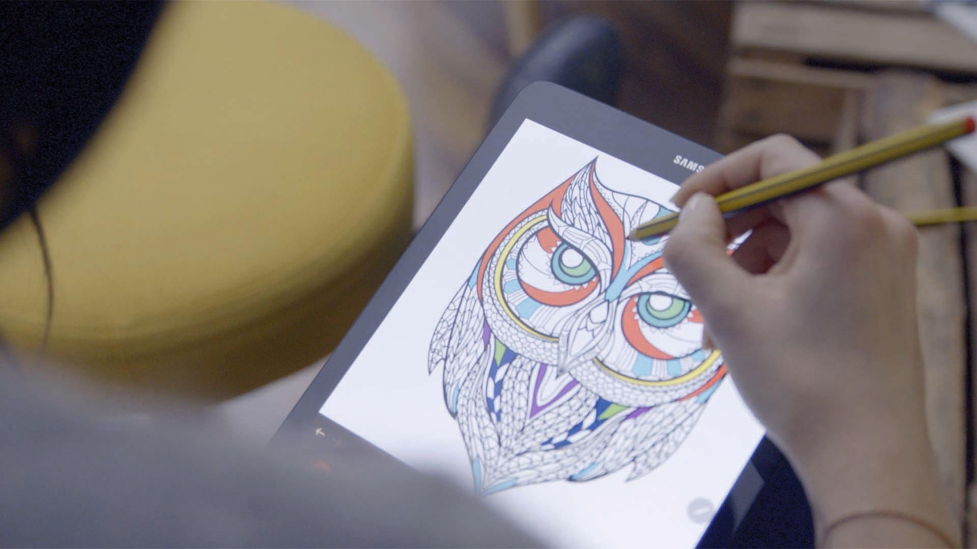 Eine Hand füllt ein detailliertes Eulenbild auf einem Tablet mit einem Stift aus.