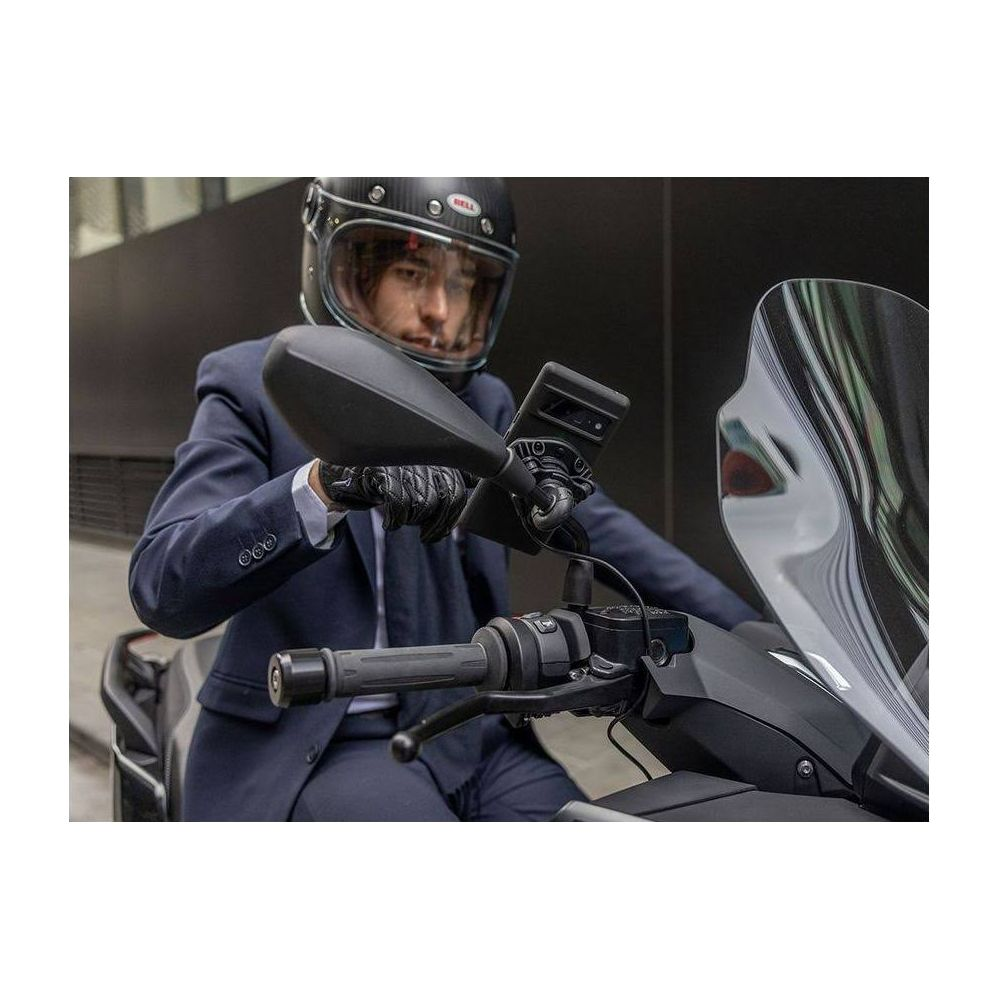 Mann in dunkelblauem Anzug und Helm sitzt auf einem Motorrad, hält Lenker und Handy.