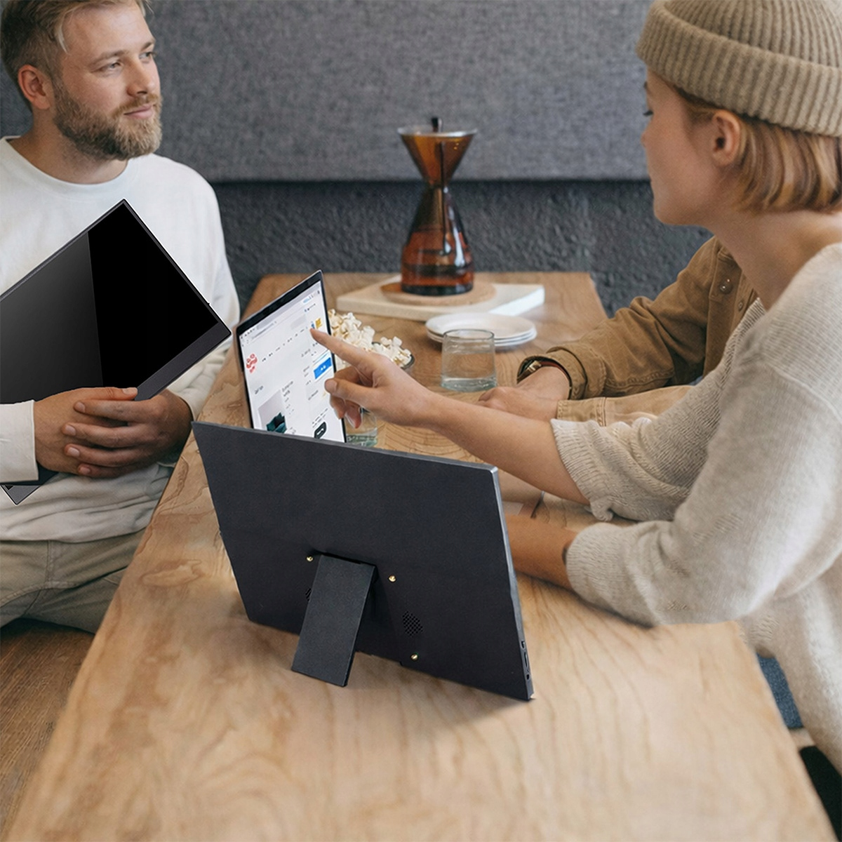 Dwie osoby przy drewnianym stole z laptopami i ekspresem do kawy w tle.