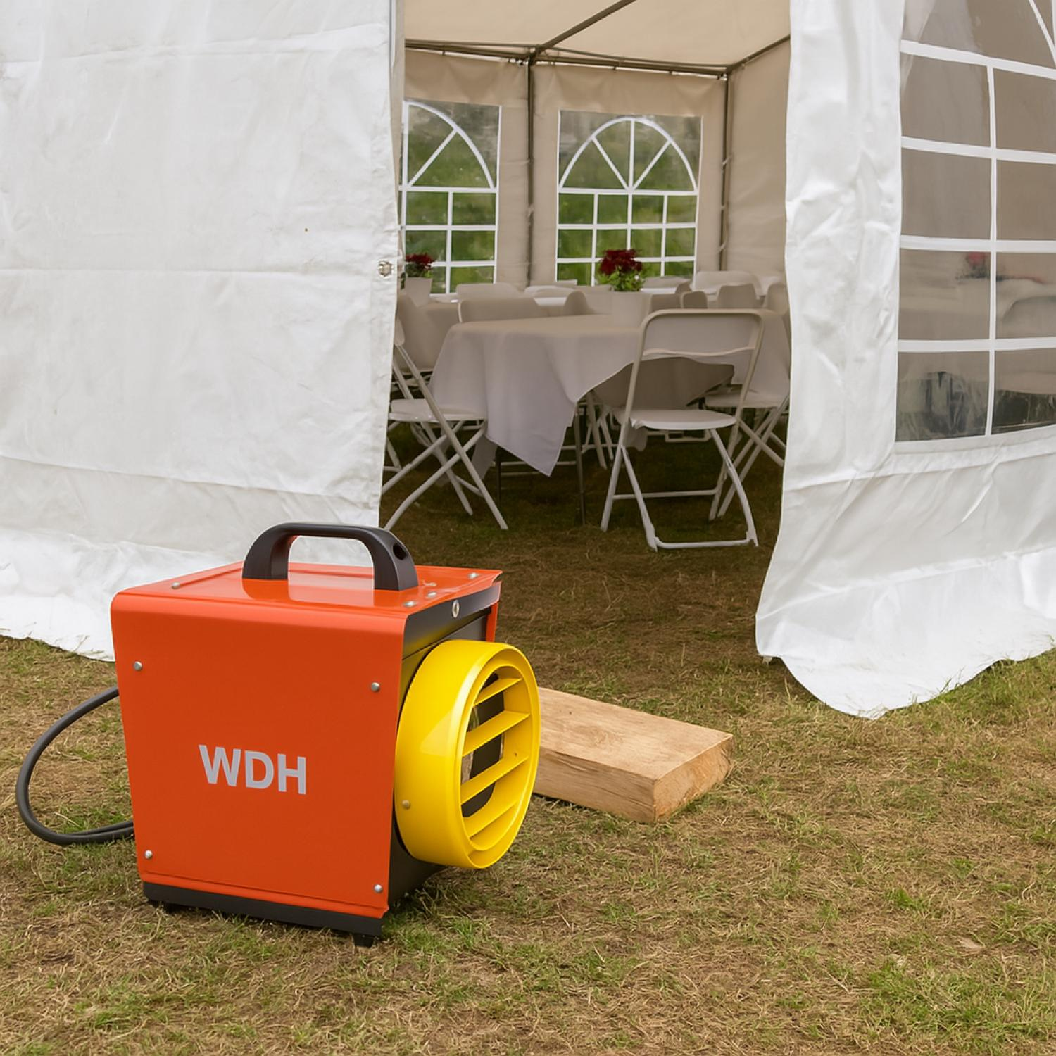 Orange WDH-Heizung mit gelbem Lüfter vor einem weißen Zelt mit Tischen und Stühlen drinnen.