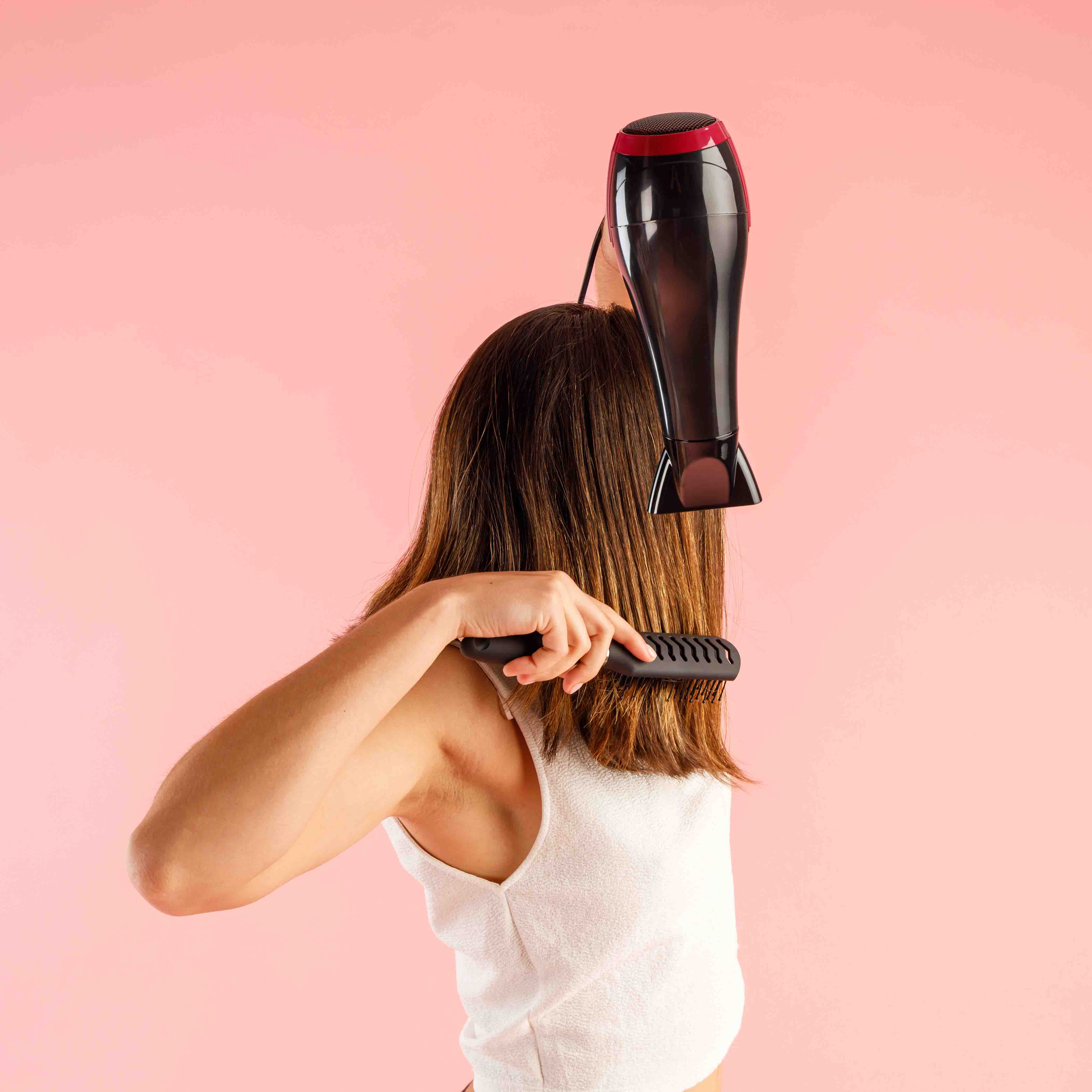 Persona secándose y peinando cabello castaño sobre fondo rosa.