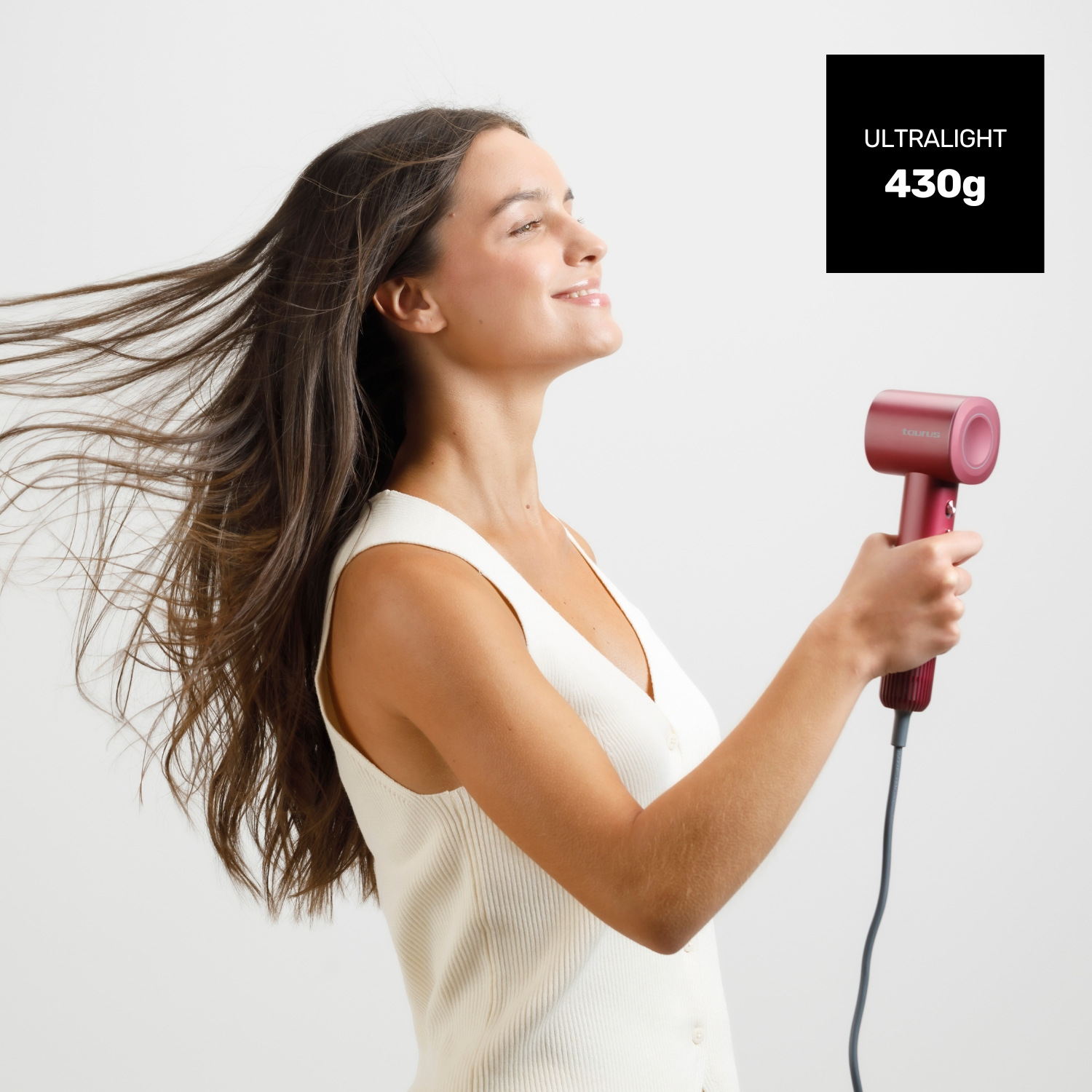 Una mujer sostiene un secador de pelo rojo, su pelo ondea al viento.