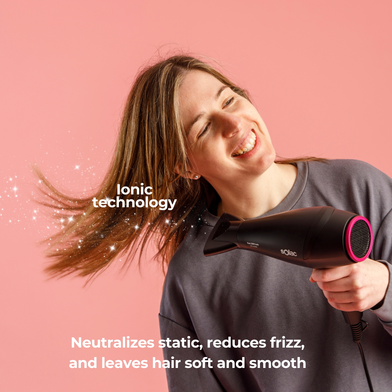 Mujer secándose el pelo con un secador negro sobre fondo rosa.