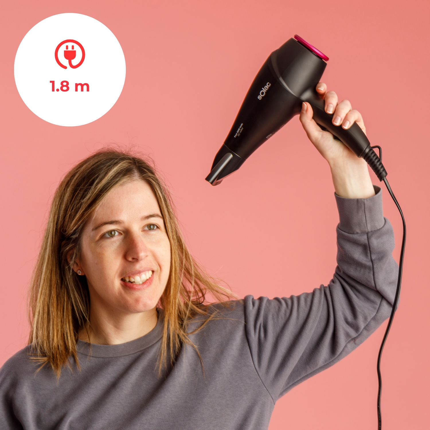 Mujer sostiene secador de pelo negro con detalle rosa sobre fondo rosa.