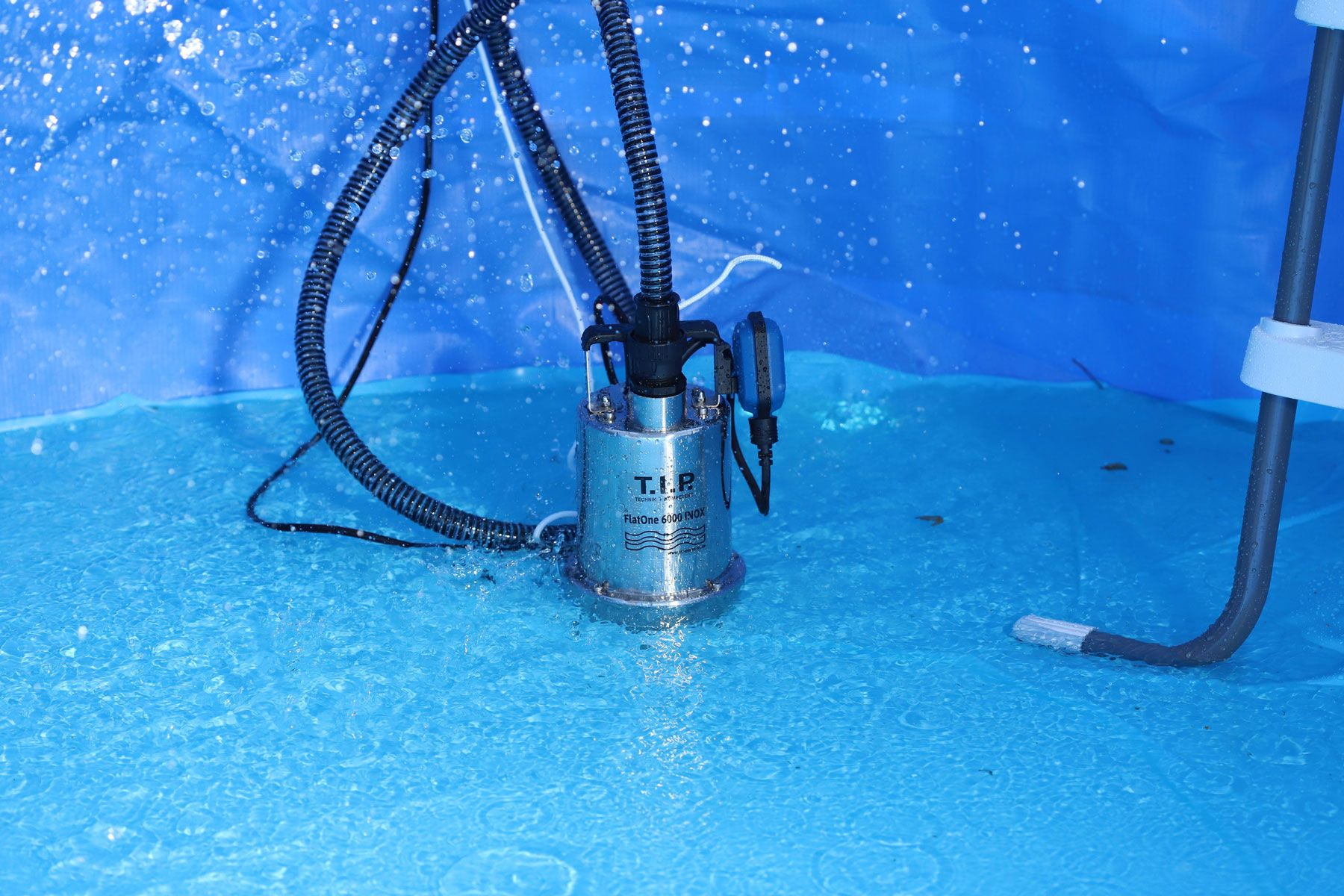 Eine Tauchpumpe arbeitet in einem blauen Pool, Wasser spritzt.