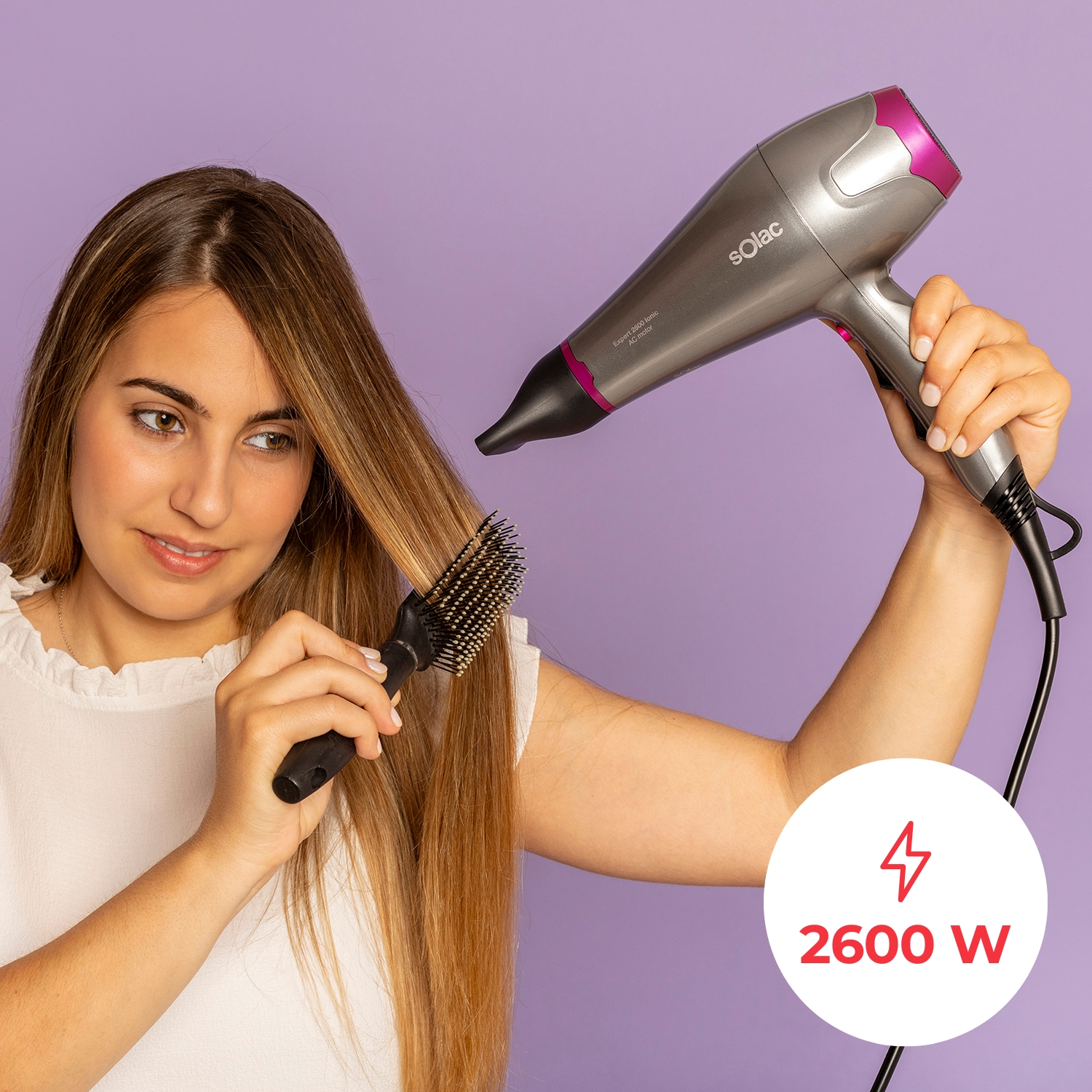 Una mujer se seca el pelo rubio con un secador plateado y rosa.