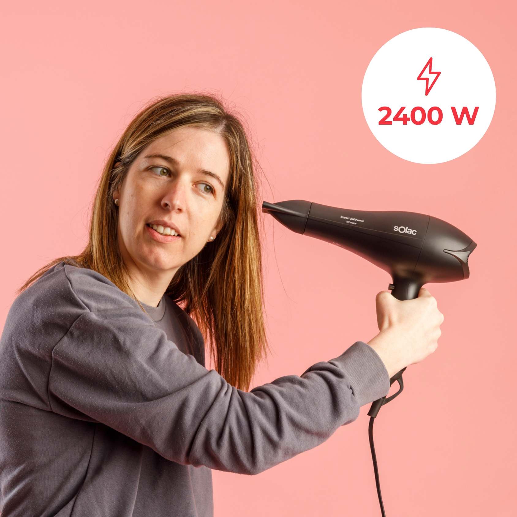 Mujer con secador de pelo negro de 2400W sobre fondo rosa.