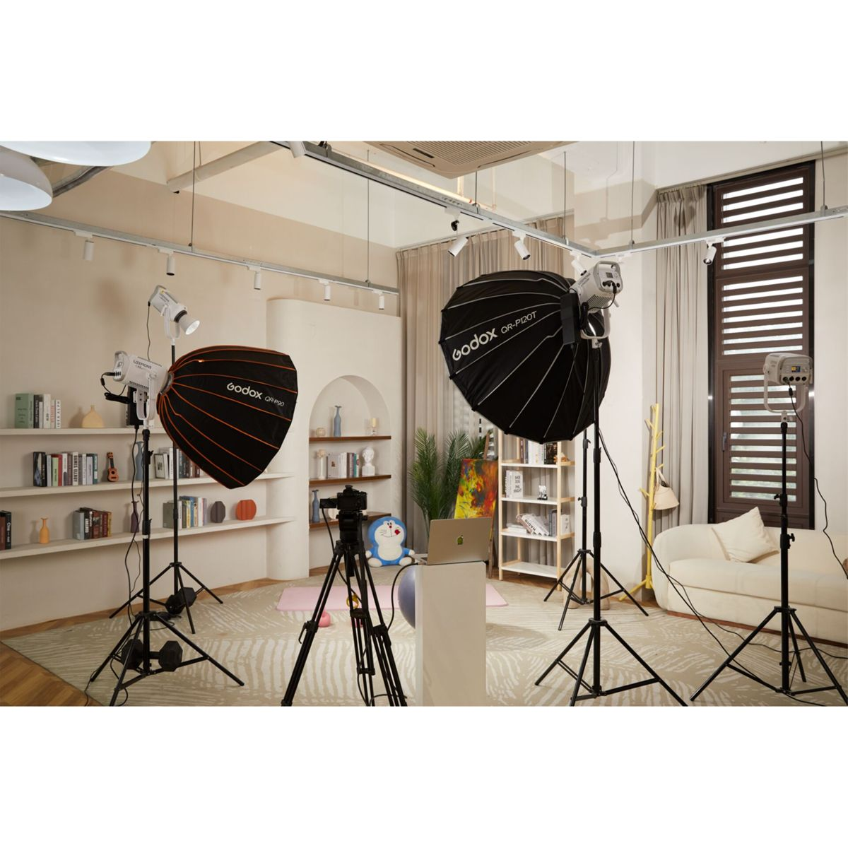 Studio mit Beleuchtung, Kamera und Stativ. Bücherregale und ein Sofa im Hintergrund.