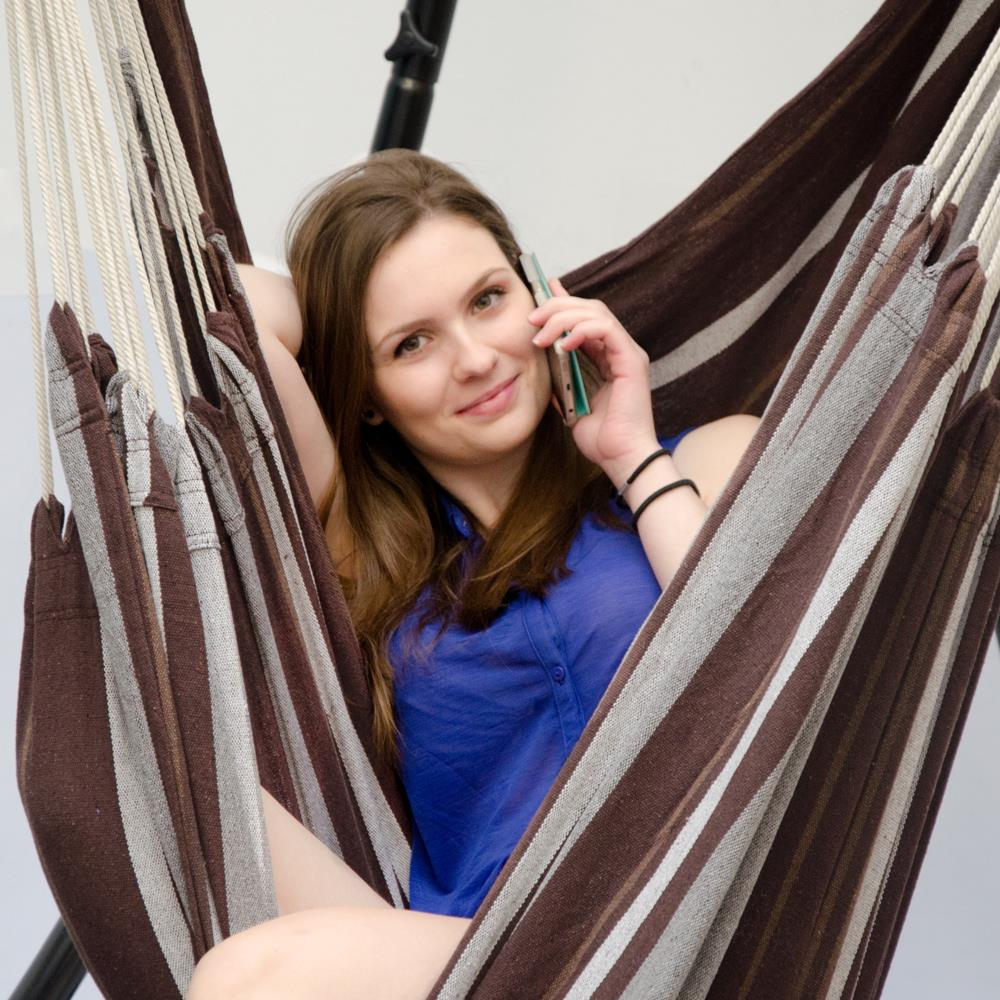 Eine Frau in einem blauen Hemd telefoniert und entspannt sich in einer gestreiften Hängematte.