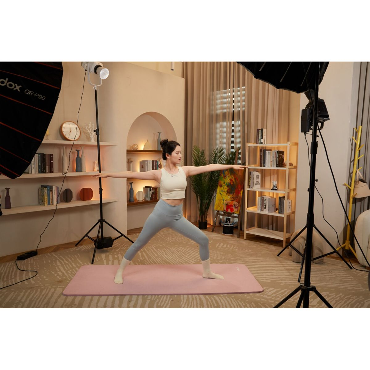 Eine Frau in sportlicher Kleidung macht Yoga auf einer rosa Matte in einem Studio mit Regalen.