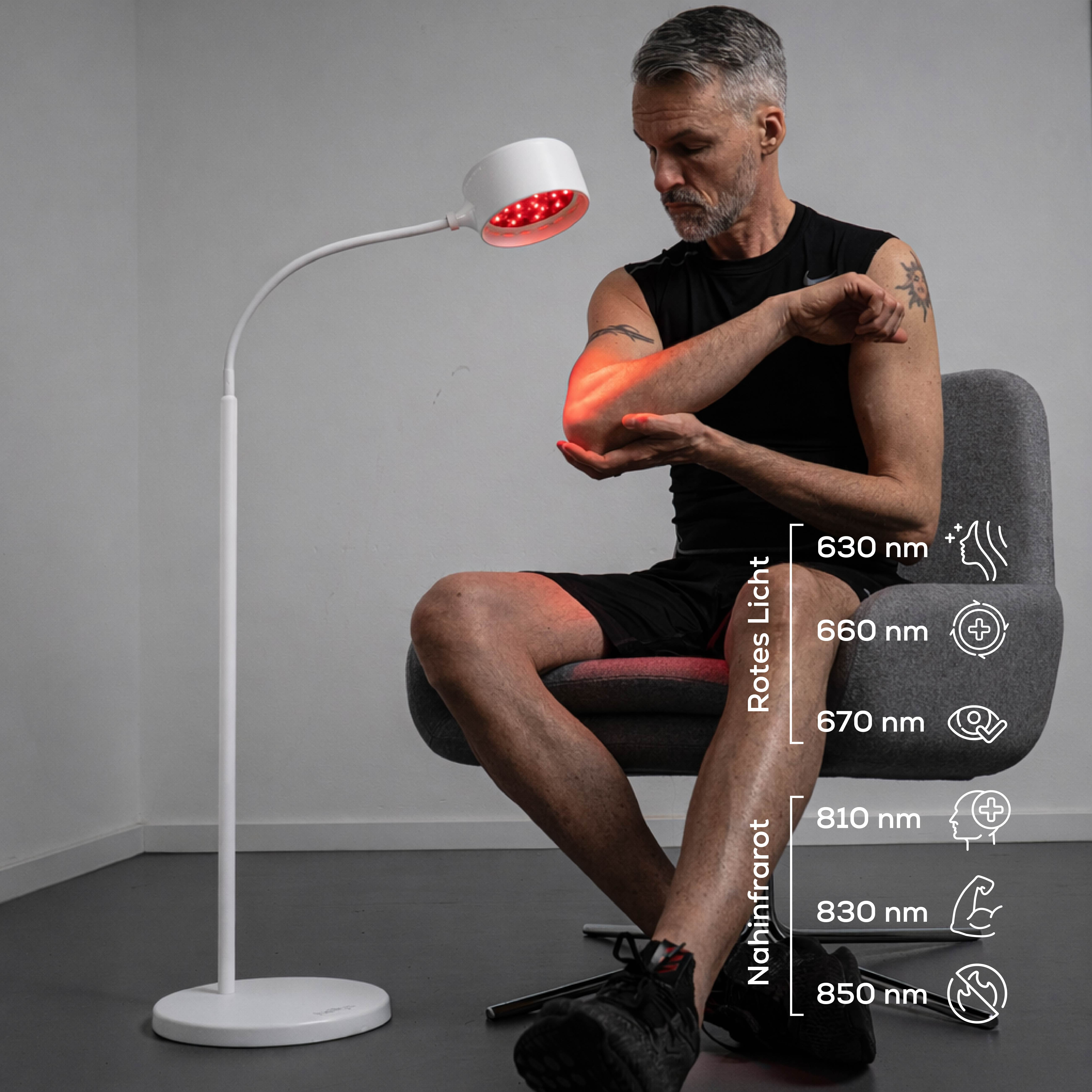 Ein Mann sitzt auf einem Stuhl, seine Arme werden von einer roten Lampe beleuchtet.