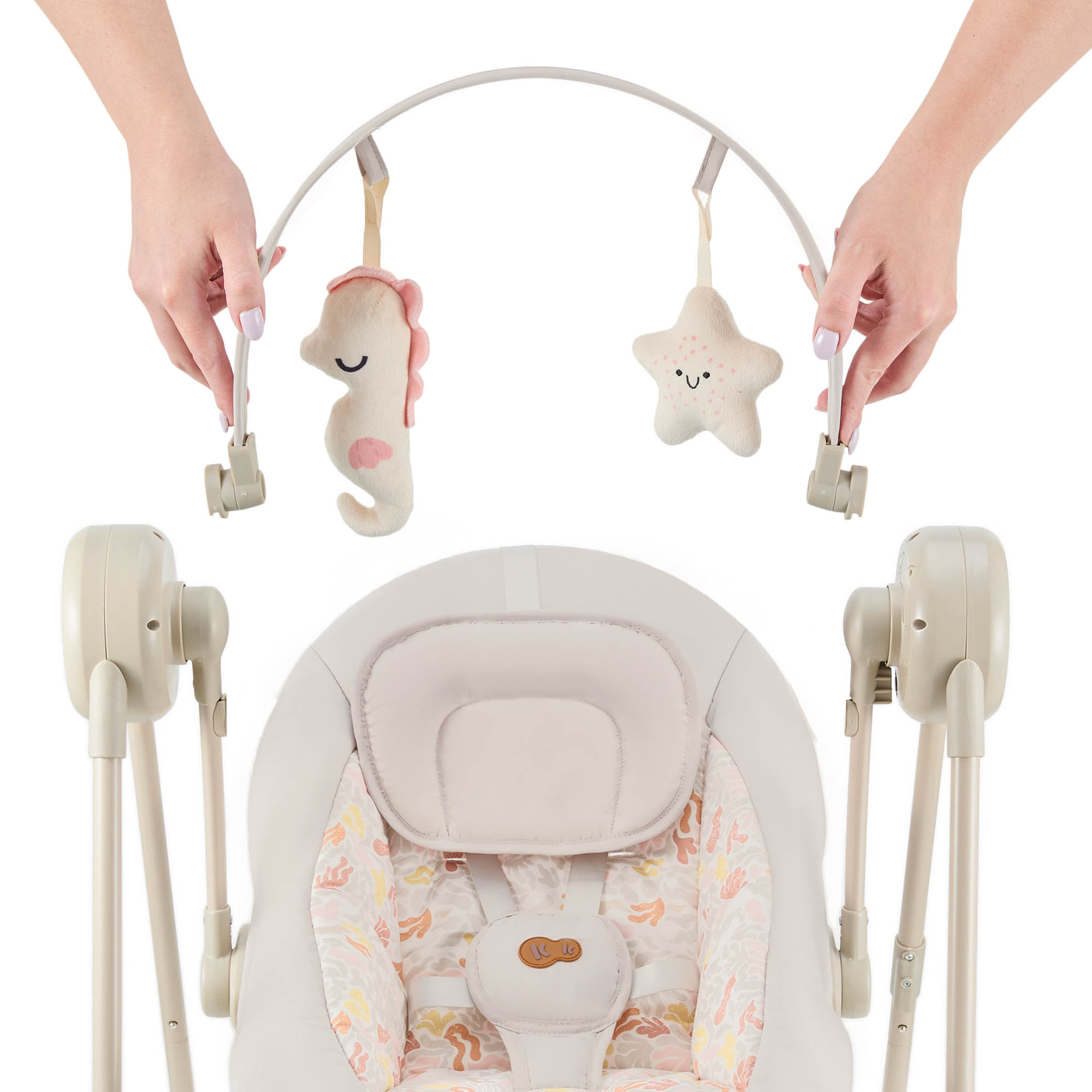 Hände befestigen einen Spielbogen mit Seepferdchen- und Sternchenspielzeug an einer Babyschaukel.