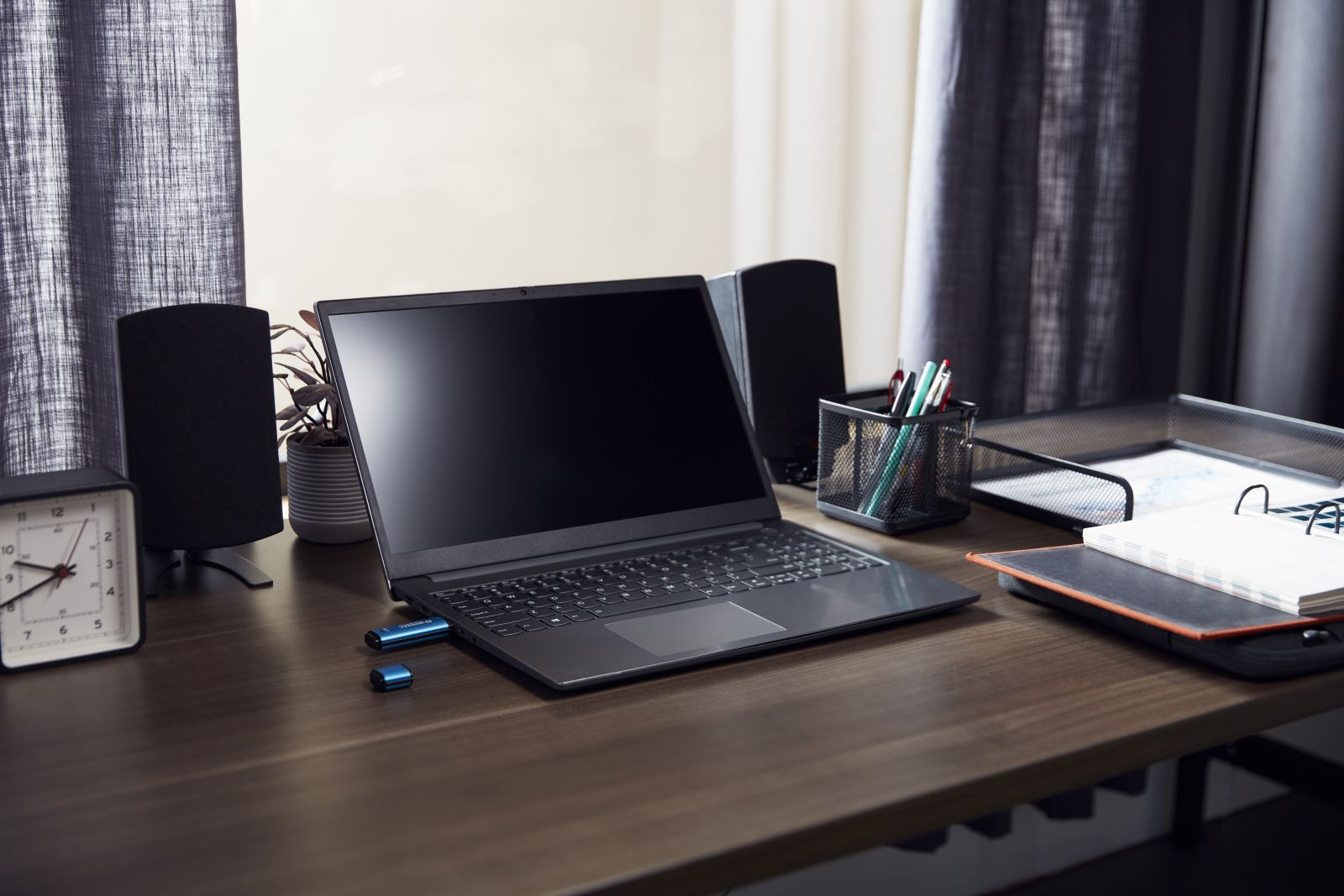 Una scrivania con laptop, altoparlanti, orologio e penne.