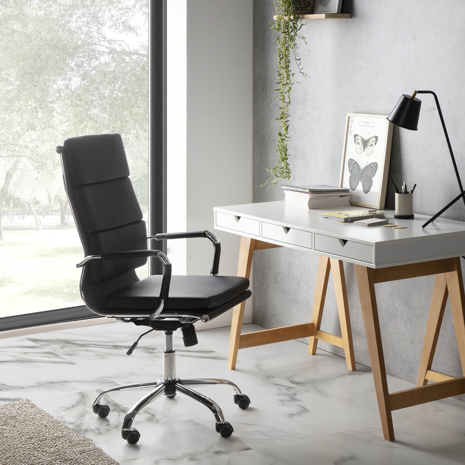 Silla de oficina de cuero negro junto a un escritorio blanco con lámpara y arte de mariposas.