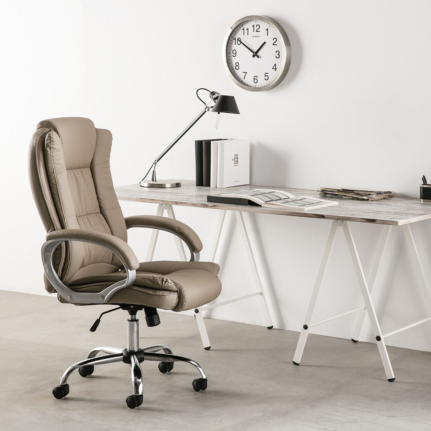 Una silla de oficina beige está frente a un escritorio con libros, una lámpara y un reloj.