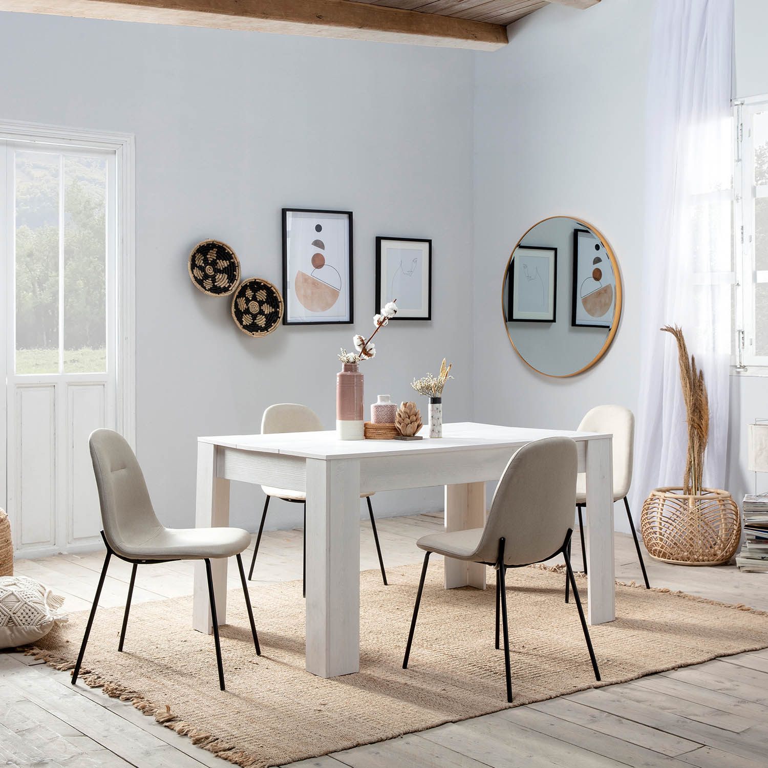 Un comedor luminoso con mesa blanca, sillas, obras de arte y un espejo redondo.