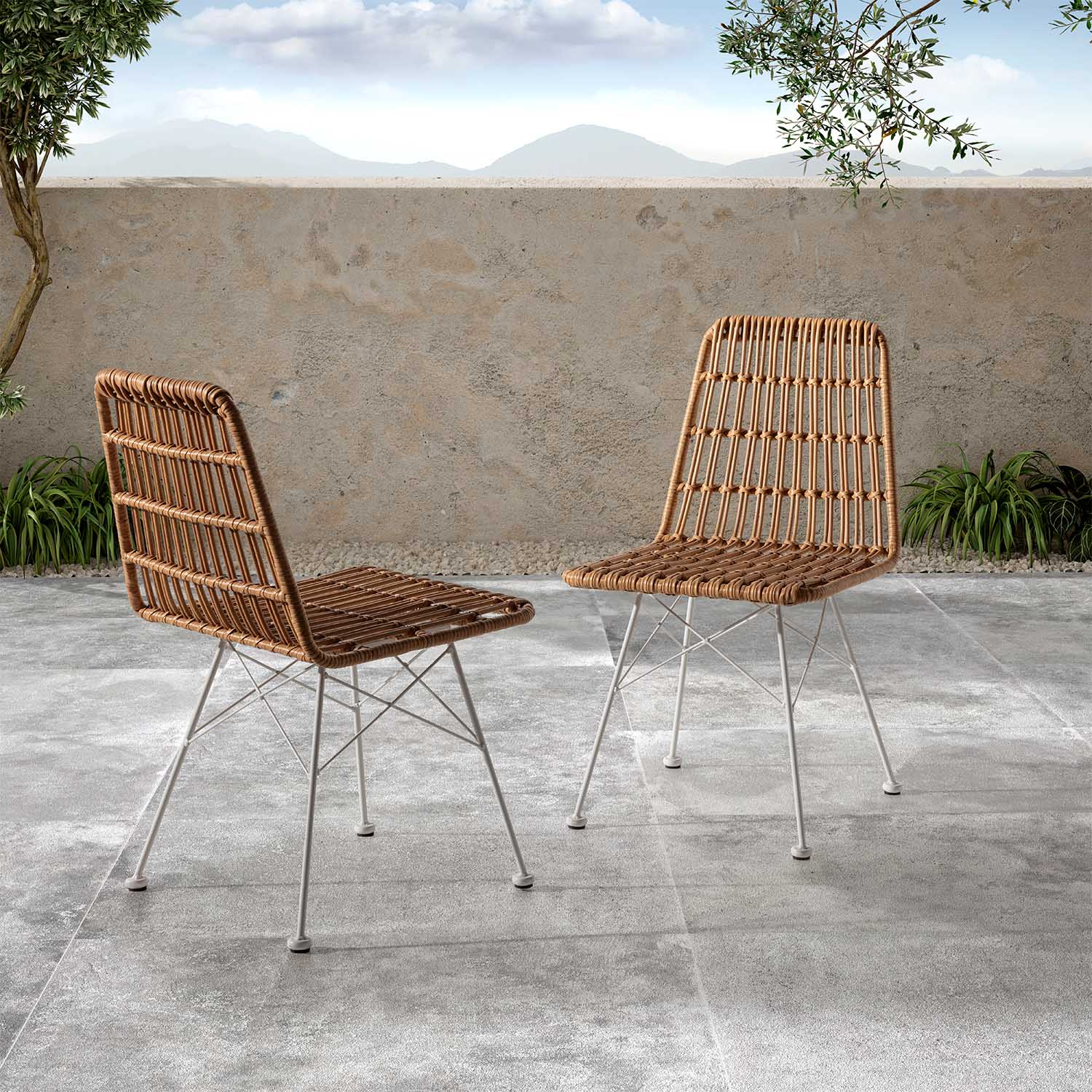 Dos sillas de mimbre con patas de metal blanco sobre un patio de piedra.