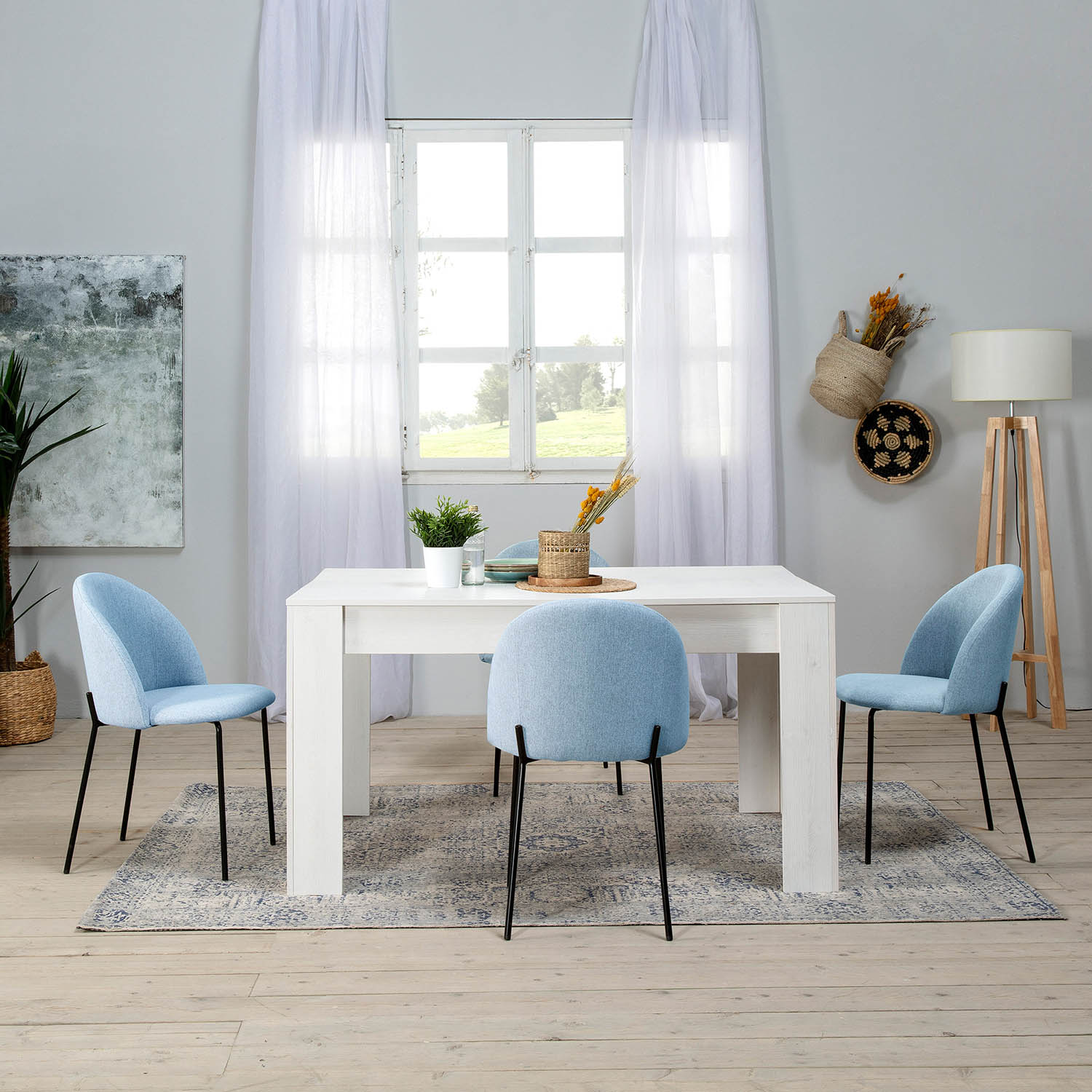 Mesa de comedor blanca con cuatro sillas azul claro, sobre una alfombra estampada.