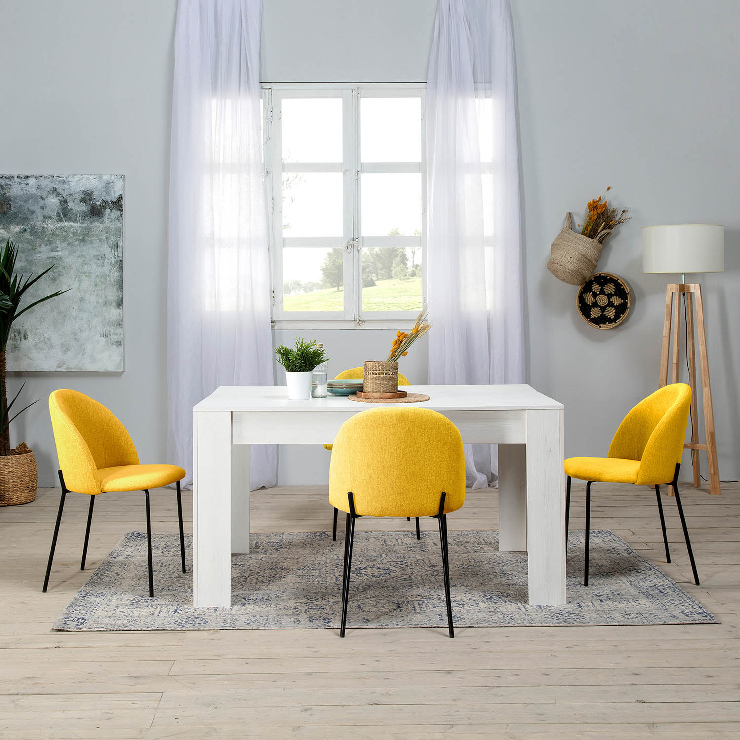 Una mesa de comedor blanca con cuatro sillas amarillas, alfombra, plantas y ventana.