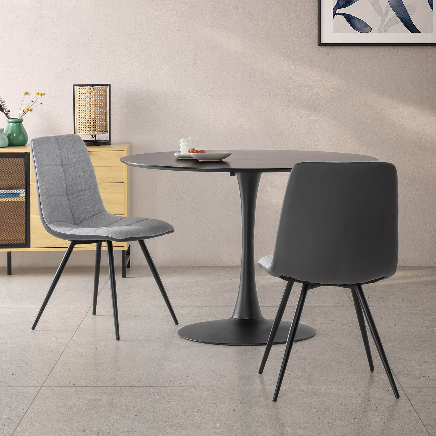 Una mesa redonda negra con dos sillas, una gris y una negra, en una habitación.