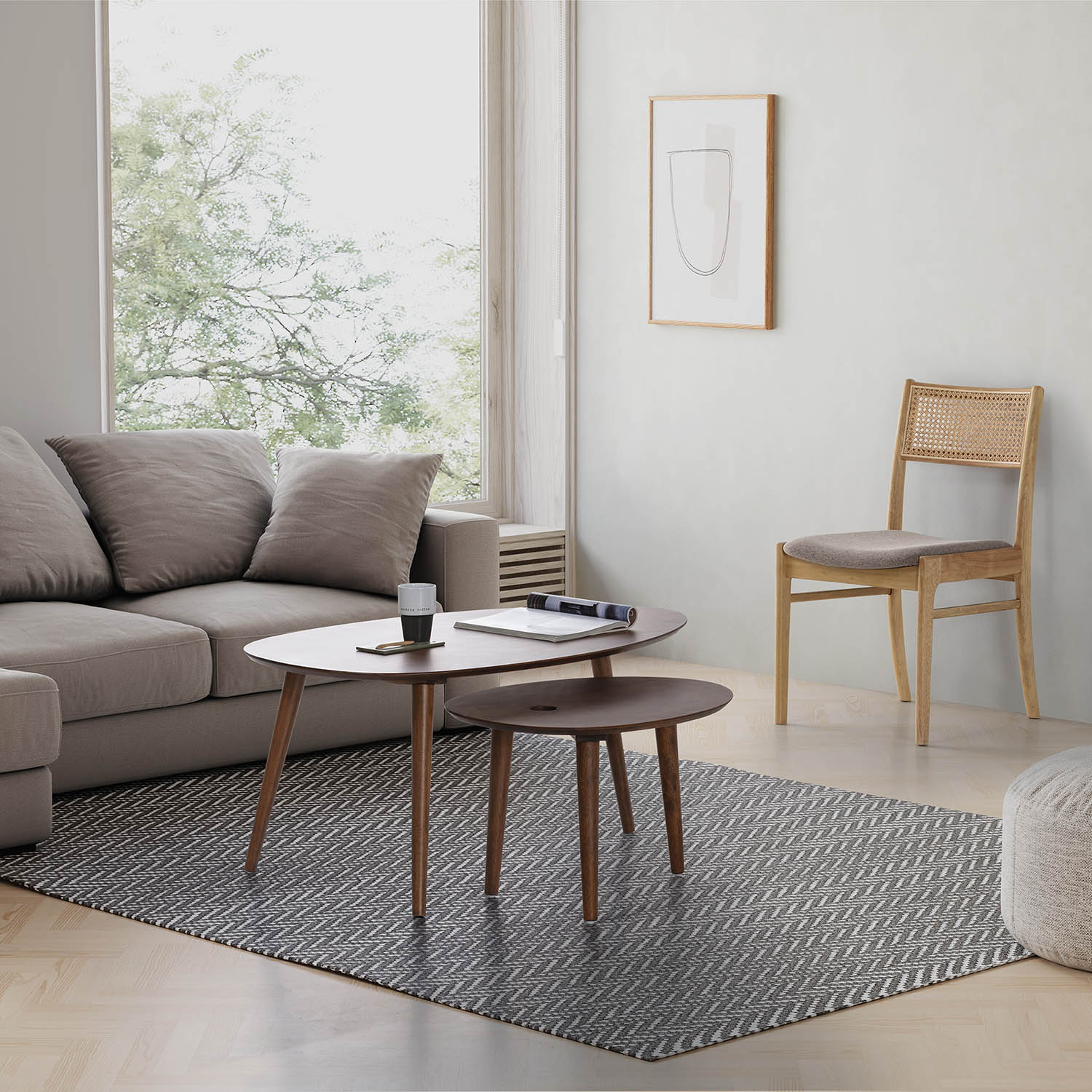 Una sala de estar moderna con sofá gris, mesas de centro ovaladas, silla tejida y alfombra estampada.