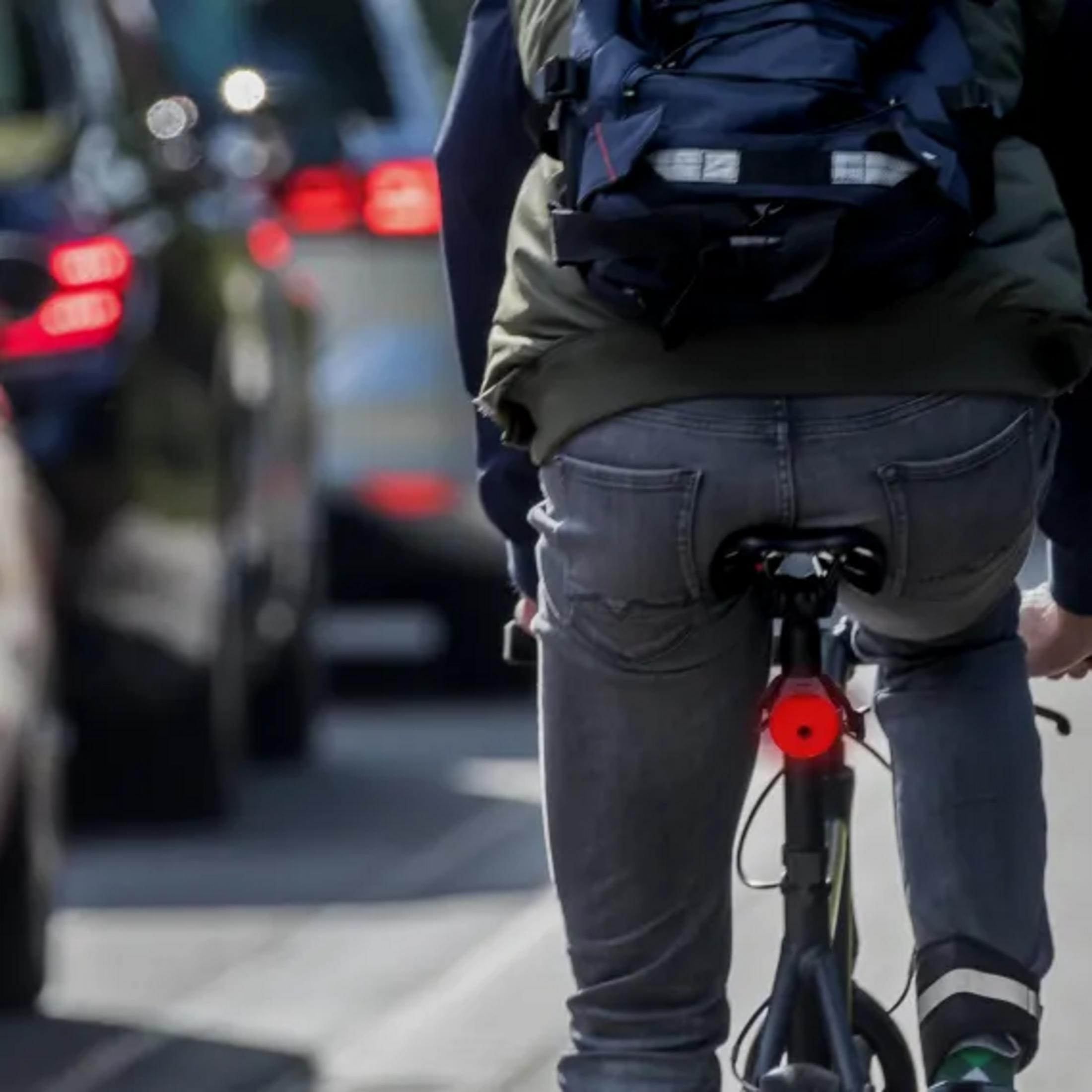 Ein Radfahrer mit Rucksack fährt im dichten Verkehr. Rücklicht ist an.