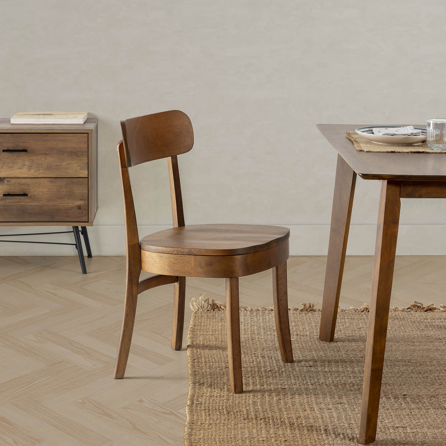 Una silla de madera junto a una mesa de madera. Una cómoda al fondo.