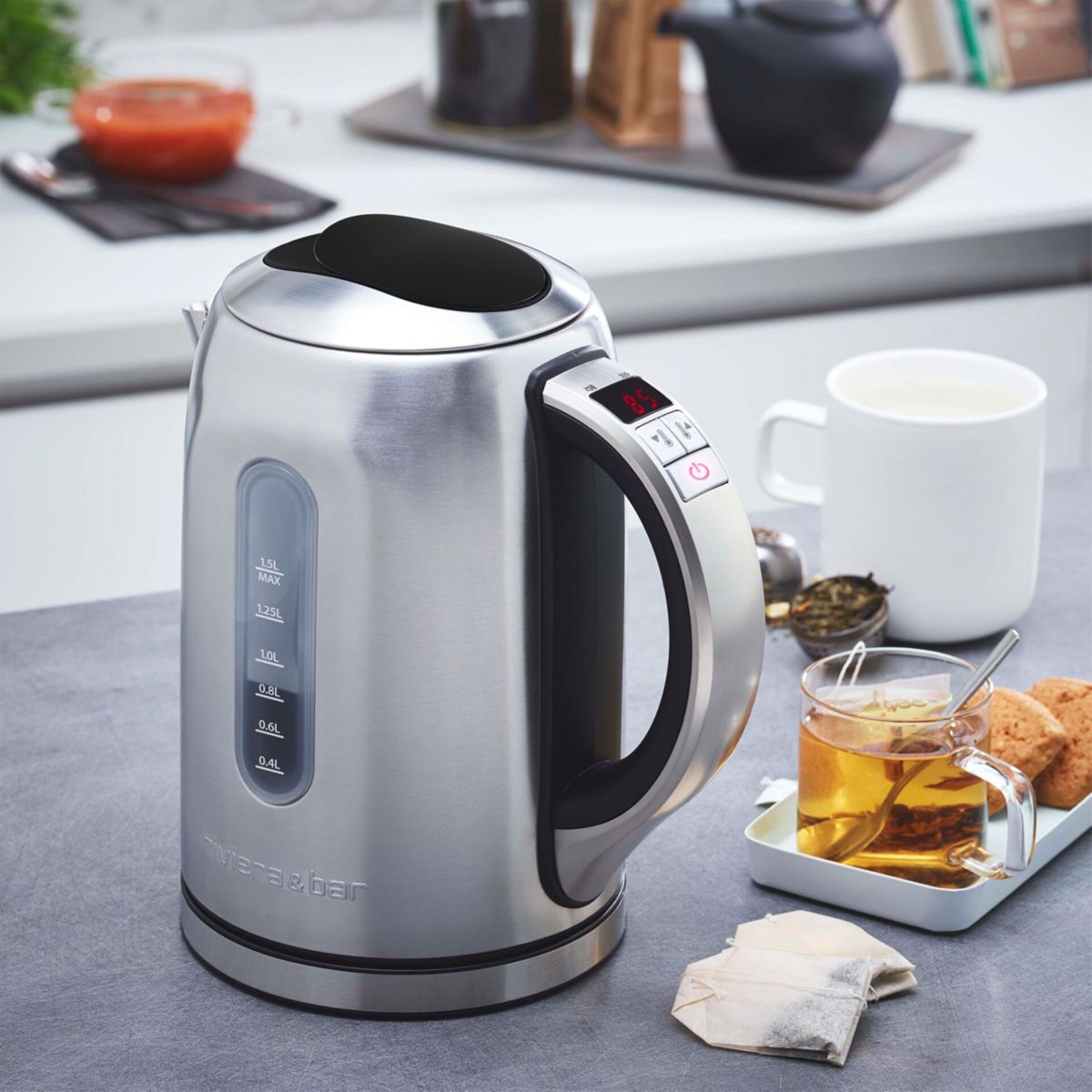 Ein silberner Wasserkocher mit digitalen Anzeigen neben einer Tasse Tee und Keksen.