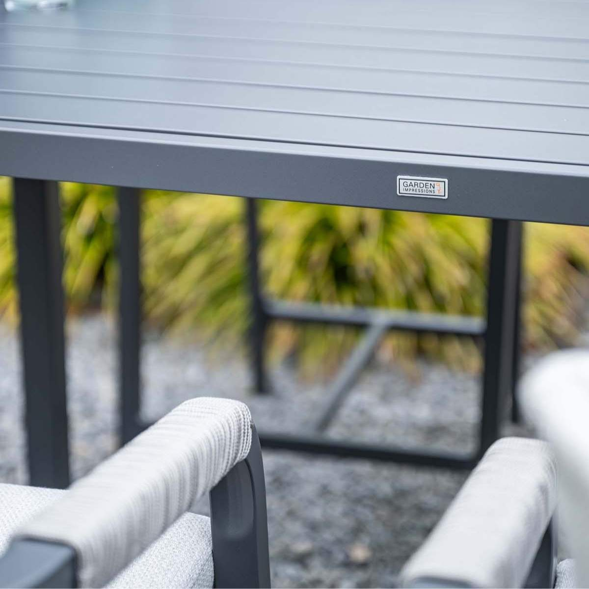 Grijze tuintafel met stoelen, bomen op de achtergrond.