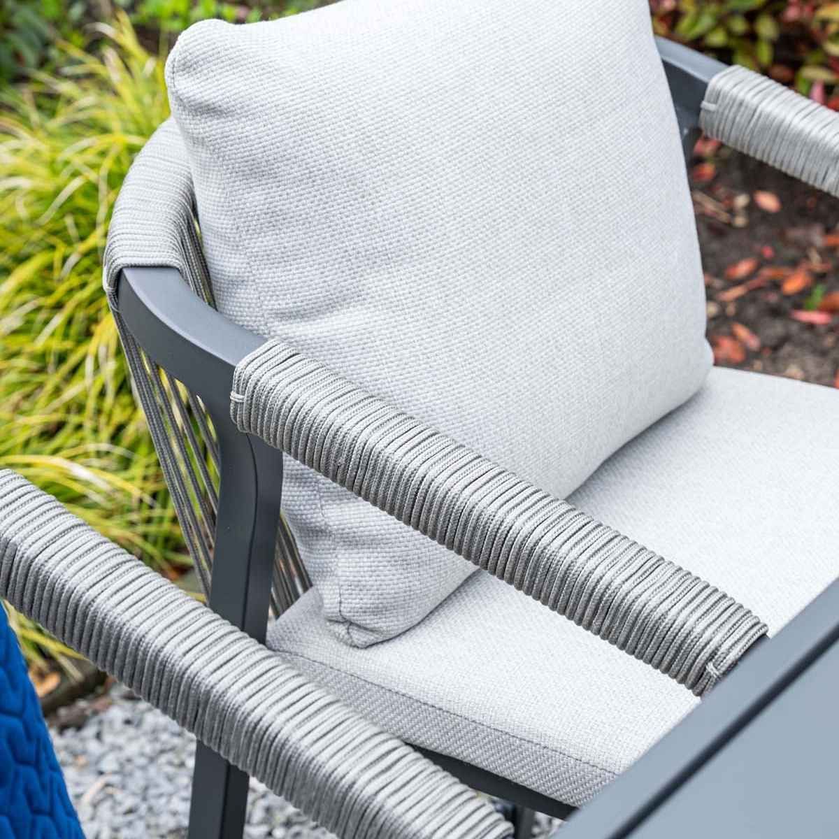 Grijze fauteuil voor buiten met kussen, planten op achtergrond.