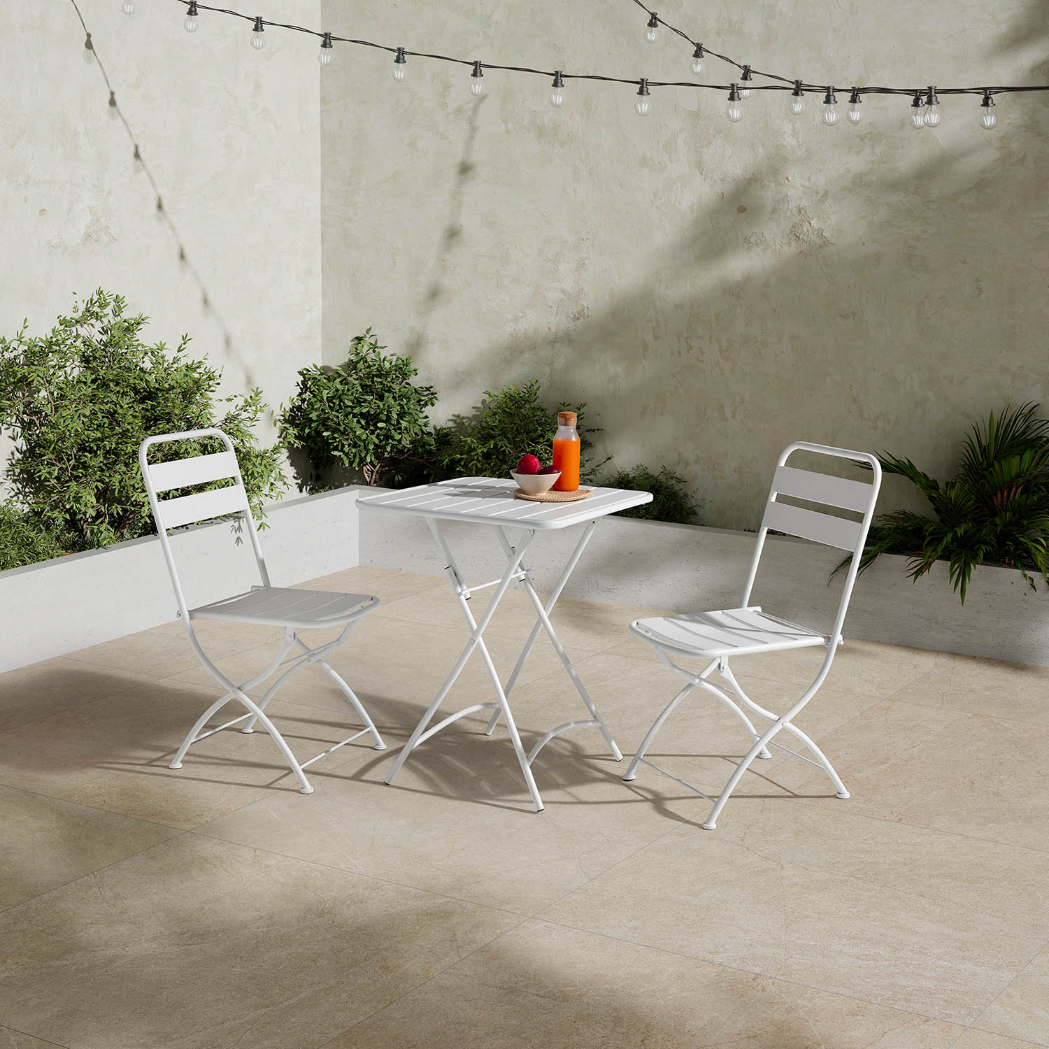 Conjunto de bistró plegable blanco con dos sillas en un patio, iluminado por luces.