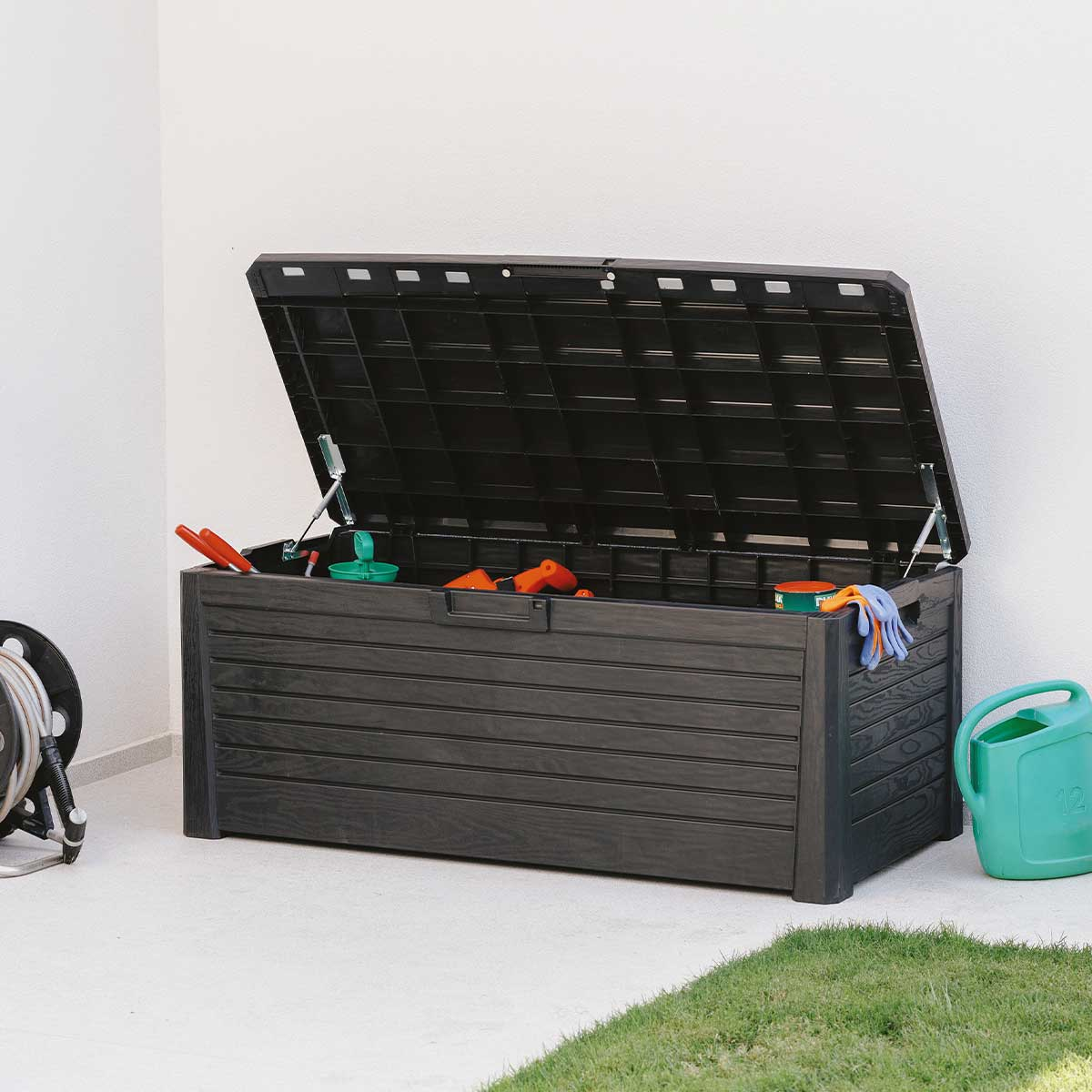Un coffre de jardin foncé avec son couvercle ouvert, rempli d'outils.