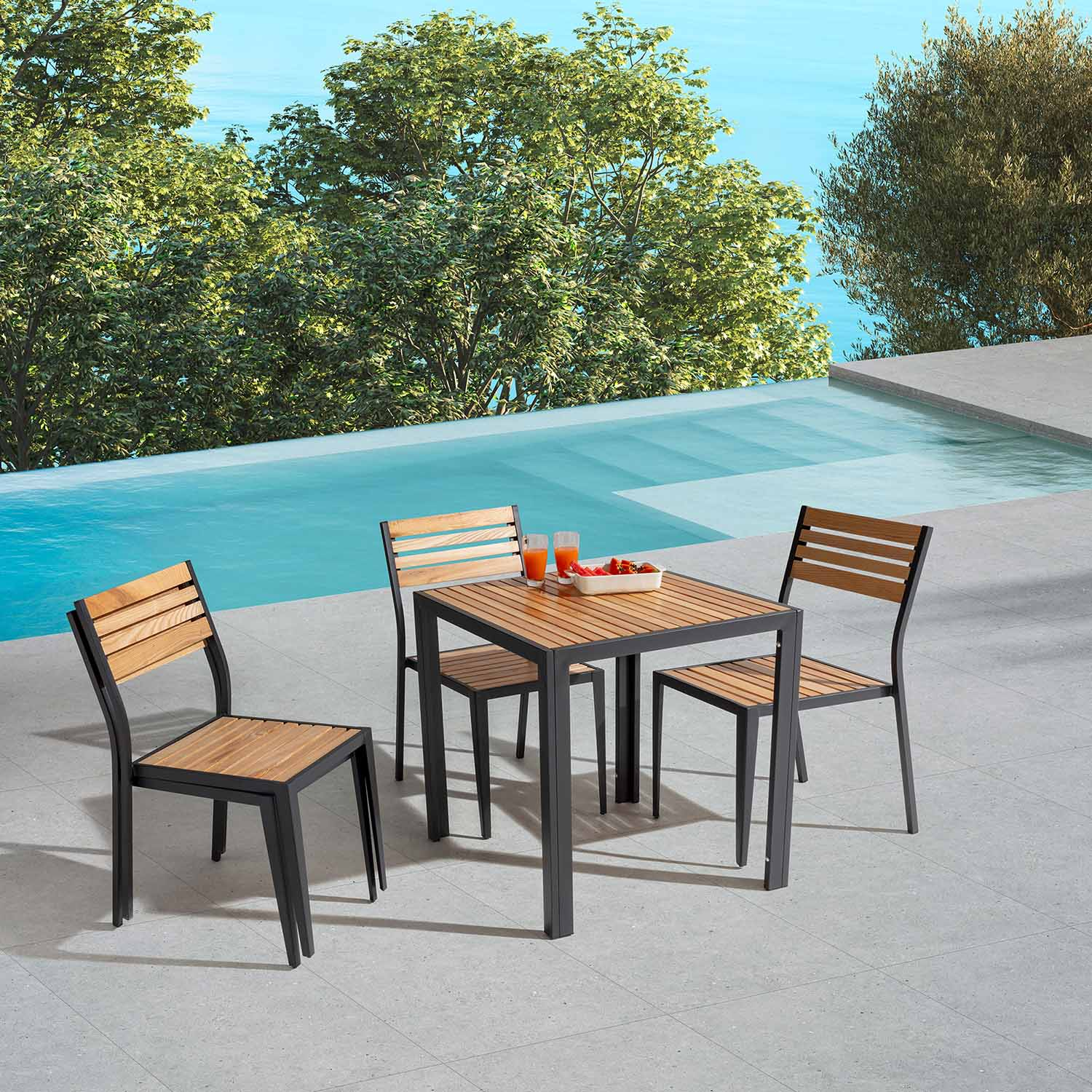 Una mesa de madera con cuatro sillas junto a una piscina, con árboles y agua al fondo.