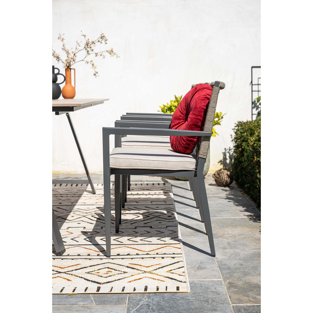 Gray outdoor chairs with cushions and red pillow on a patio with a rug.