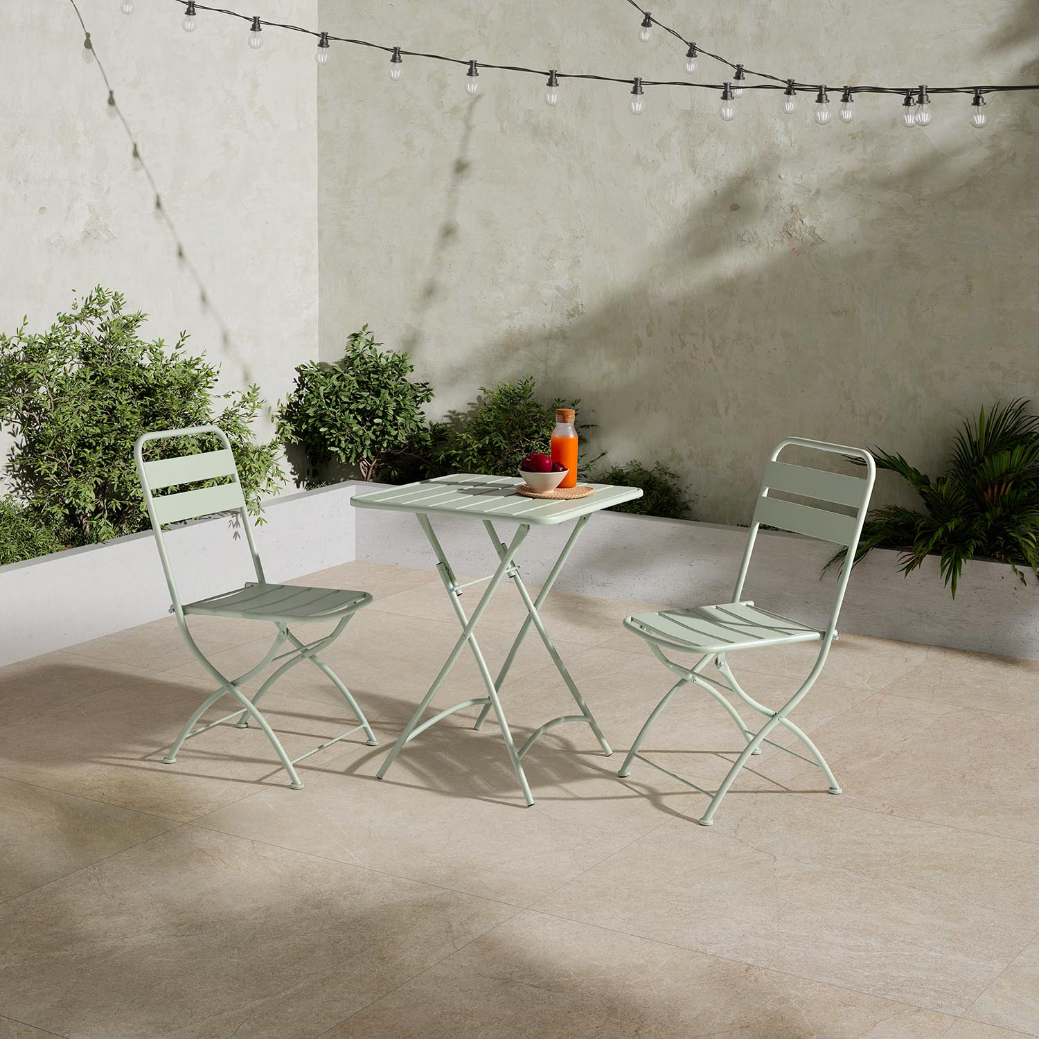 Un juego de mesa de jardín verde claro con dos sillas en un patio bajo luces de cadena.